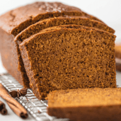A loaf of gluten free pumpkin bread is sliced and sitting on top of a grated cooling tray.