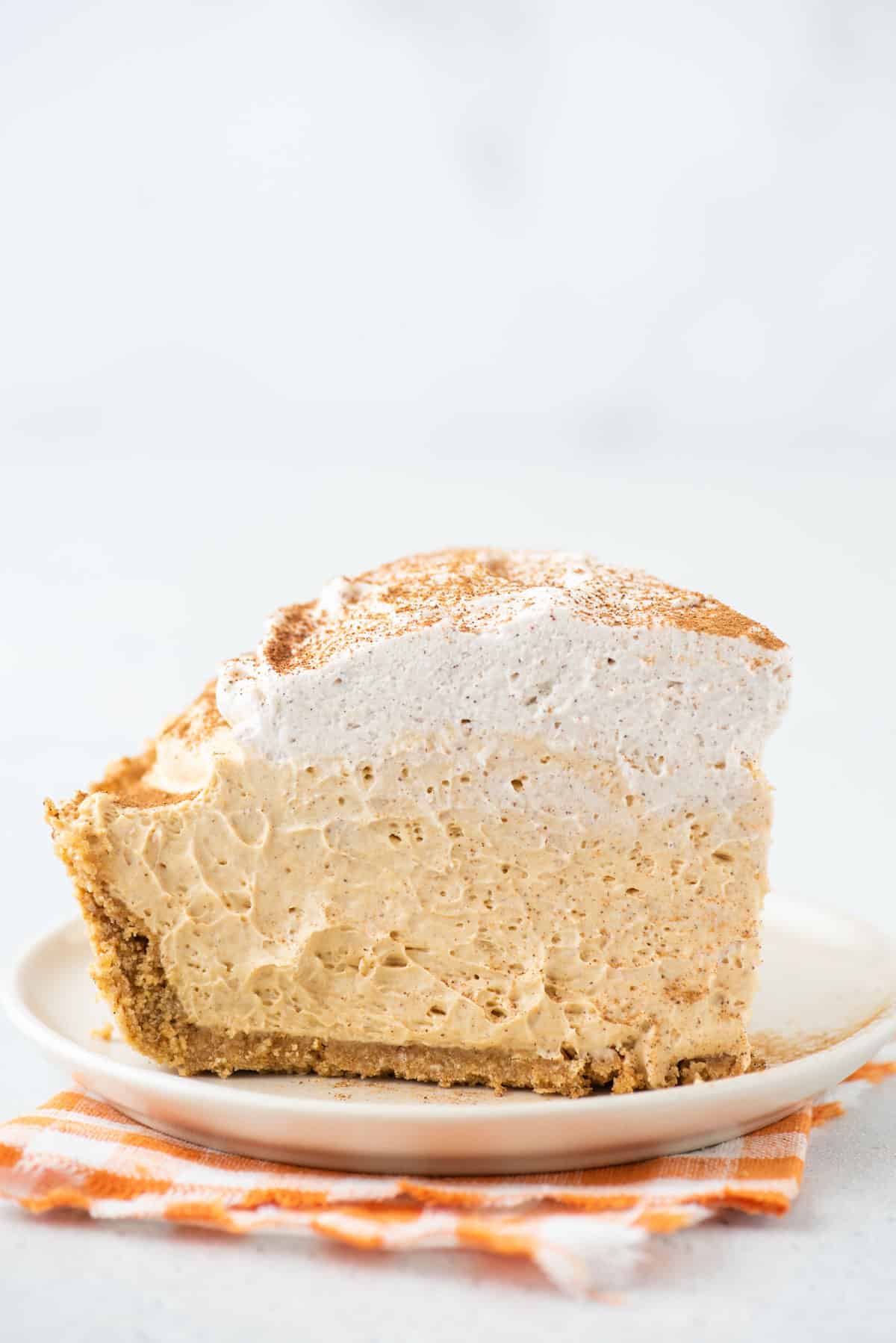 A tall slice of no bake pumpkin pie sits on a white plate.