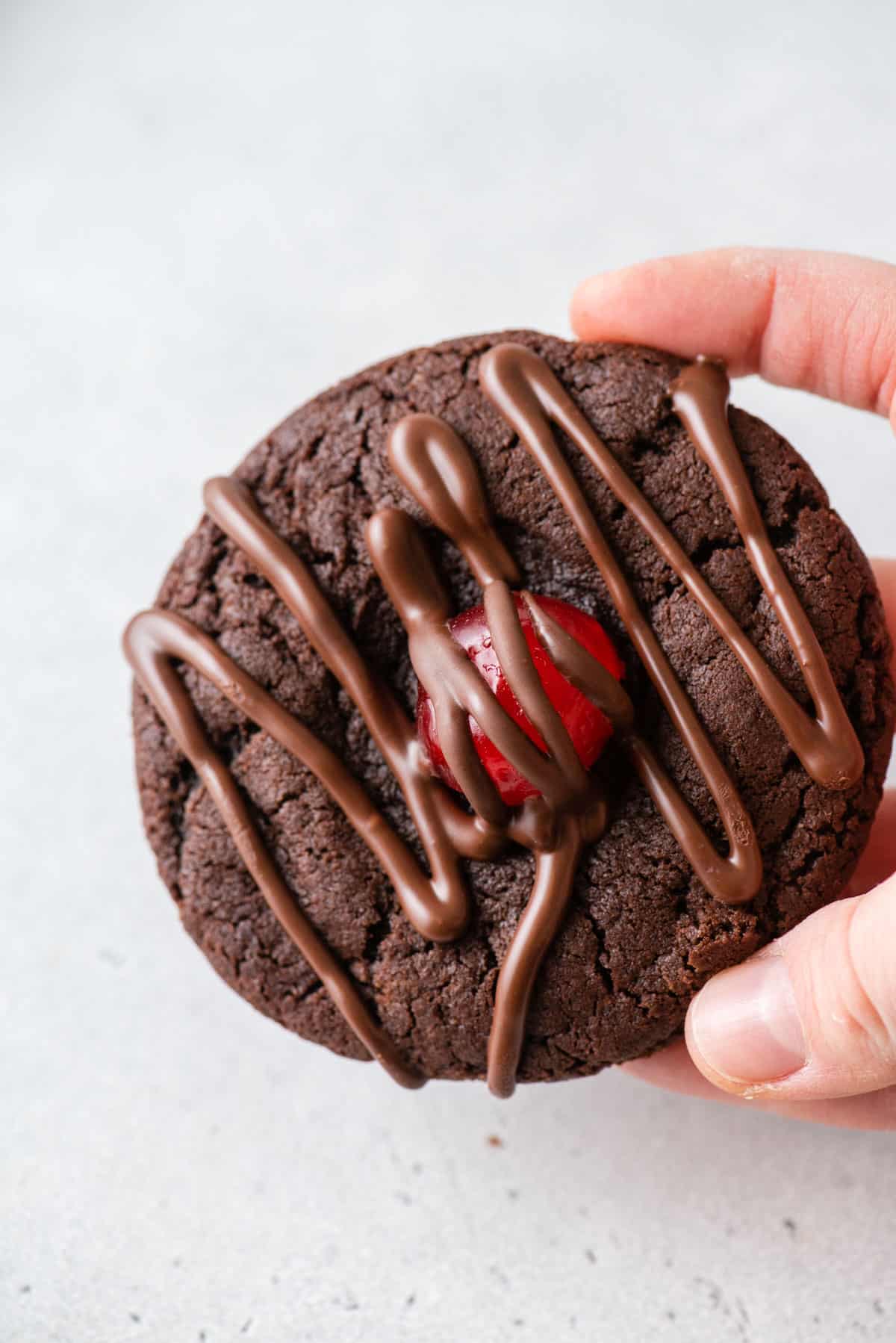A hand holding a chocolate cherry cookie