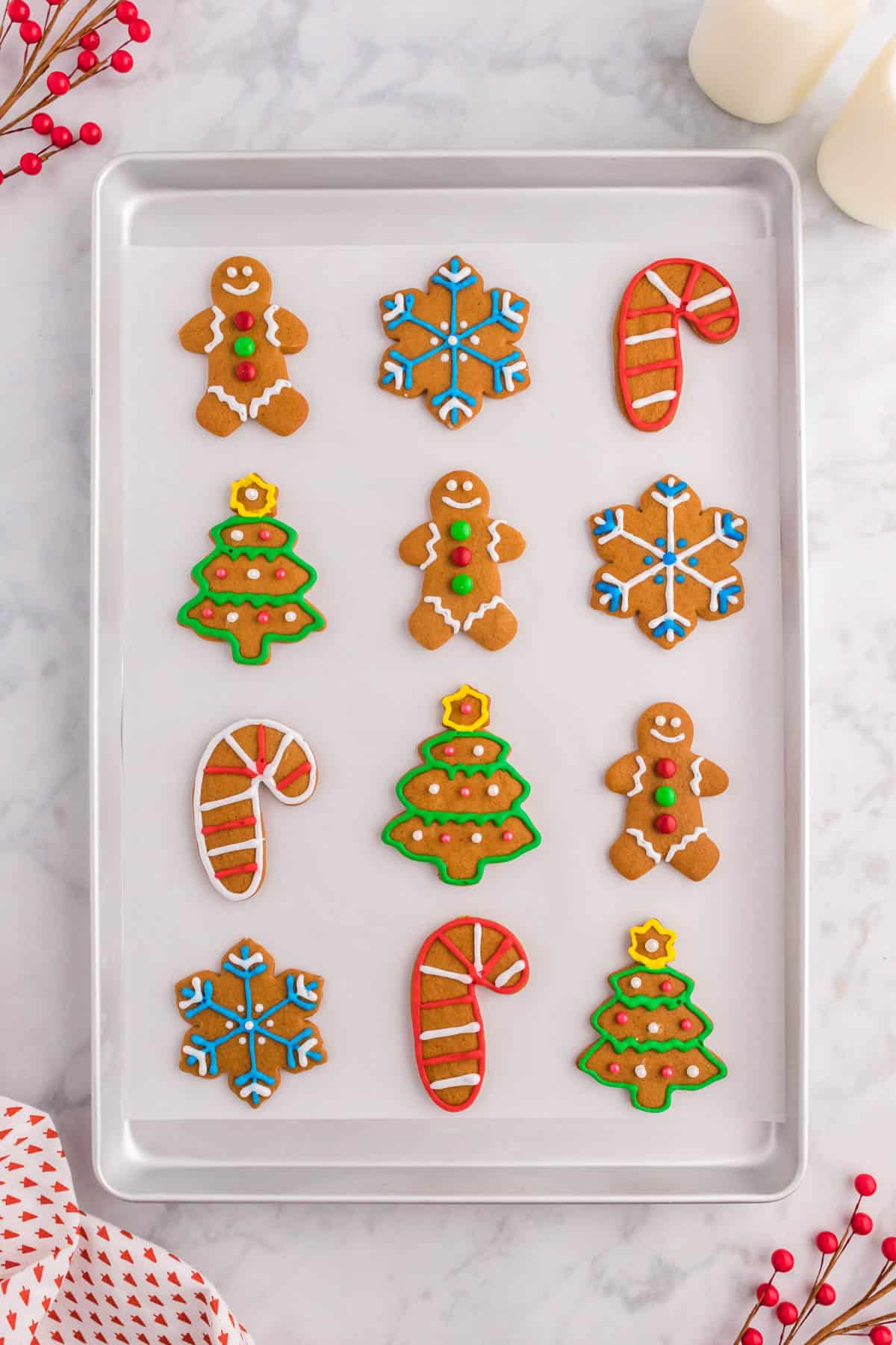 12 gingerbread cut out cookies decorated and arranged in grid pattern on baking sheet
