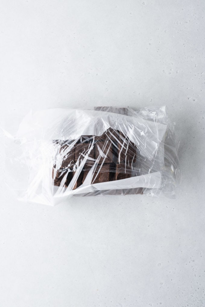 chocolate fudge with parchment paper between layers wrapped in plastic wrap