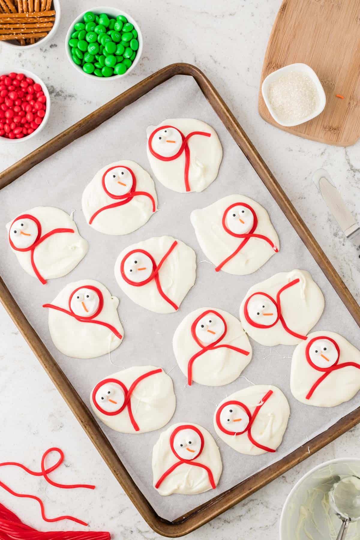 dollops of melted white chocolate arranged in grid on parchment paper with snowman faces