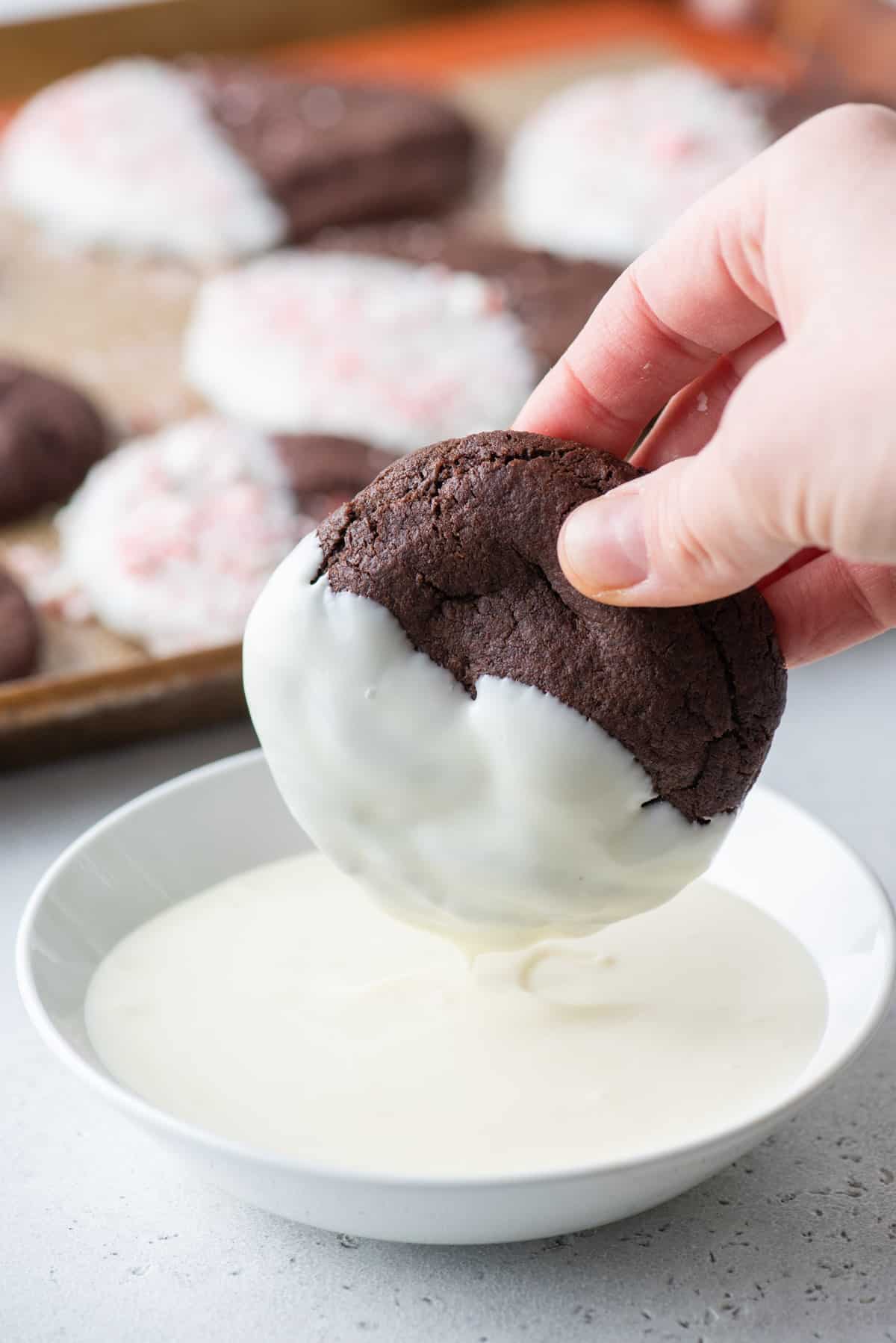 A hand dipping a chocolate cookie into melted white chocolate