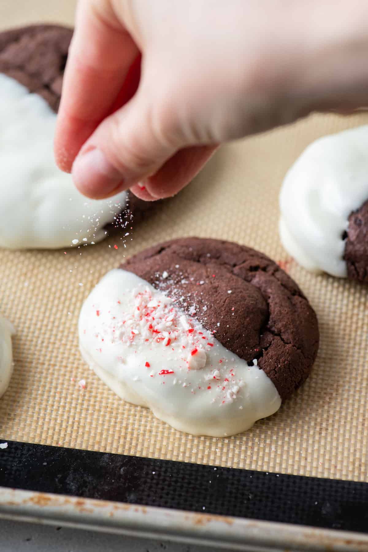 A hand sprinkling crushed candy canes over a cookie