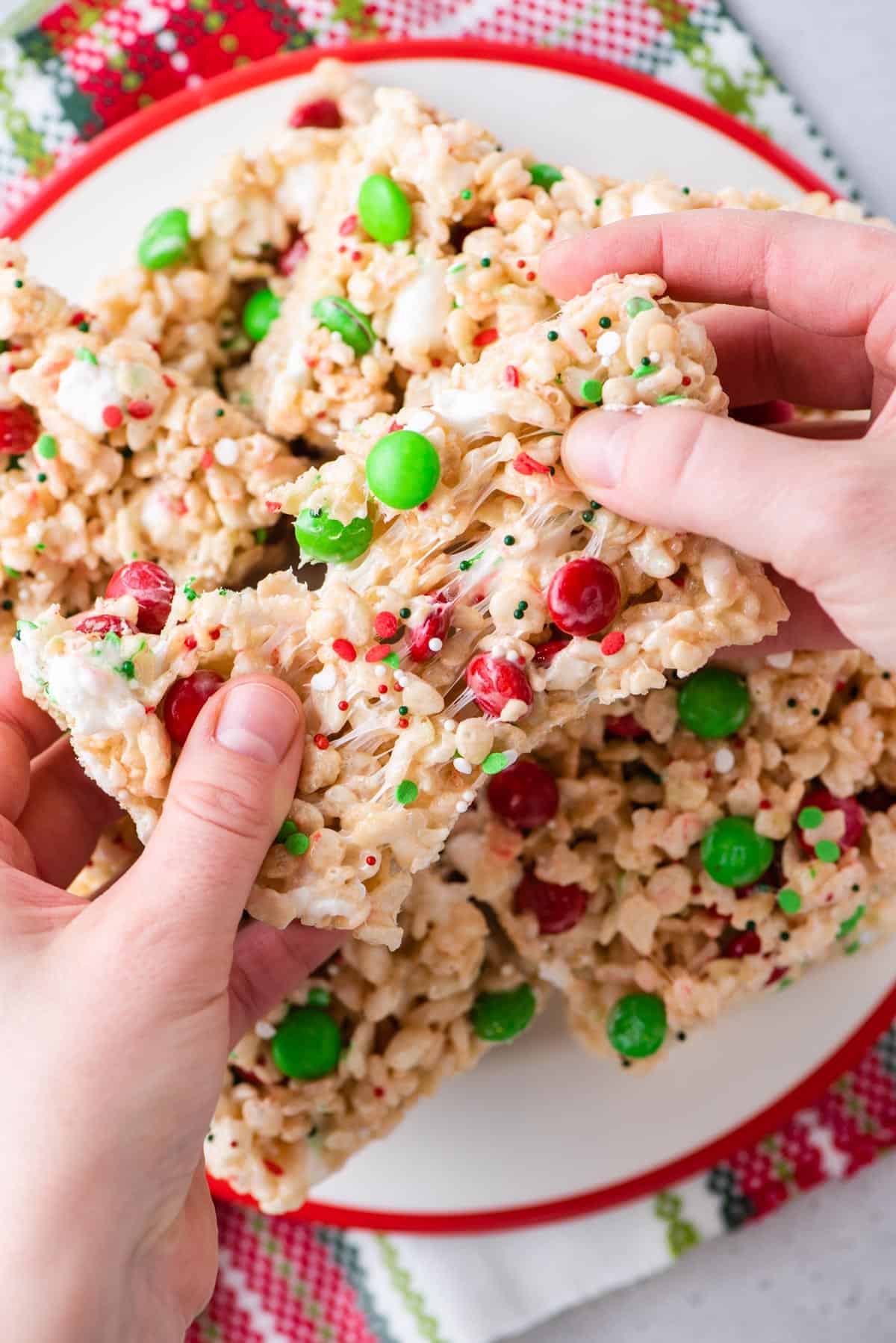 A hand grabbing two Christmas rice krispie treats from a white plate