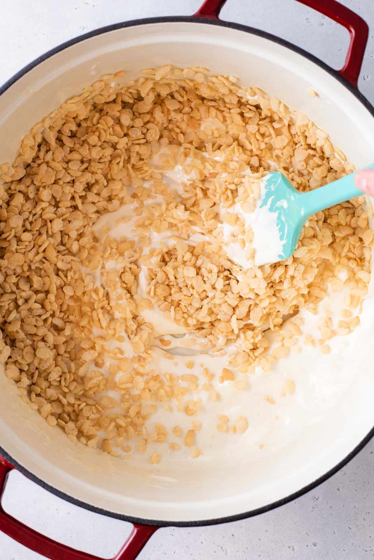 A blue spatula stirring Rice Krispie cereal into melted marshmallows