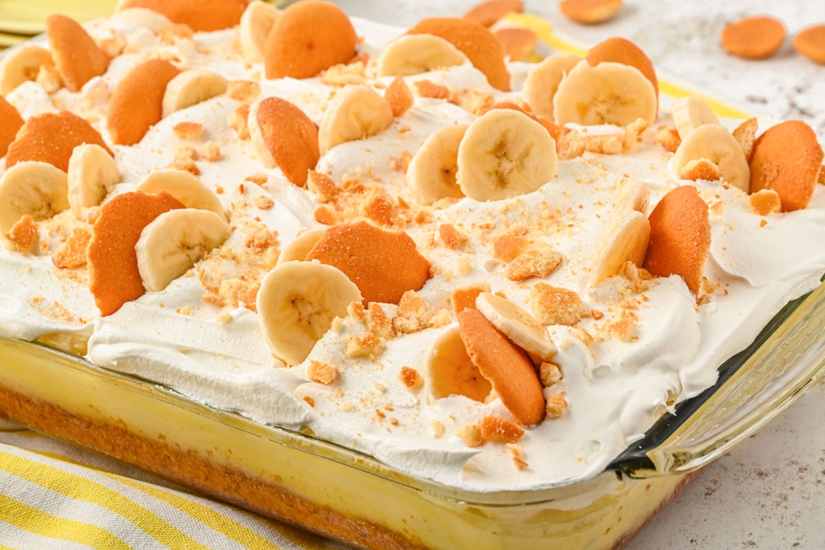 banana poke cake in a baking dish sitting on a white and yellow striped towel on a counter
