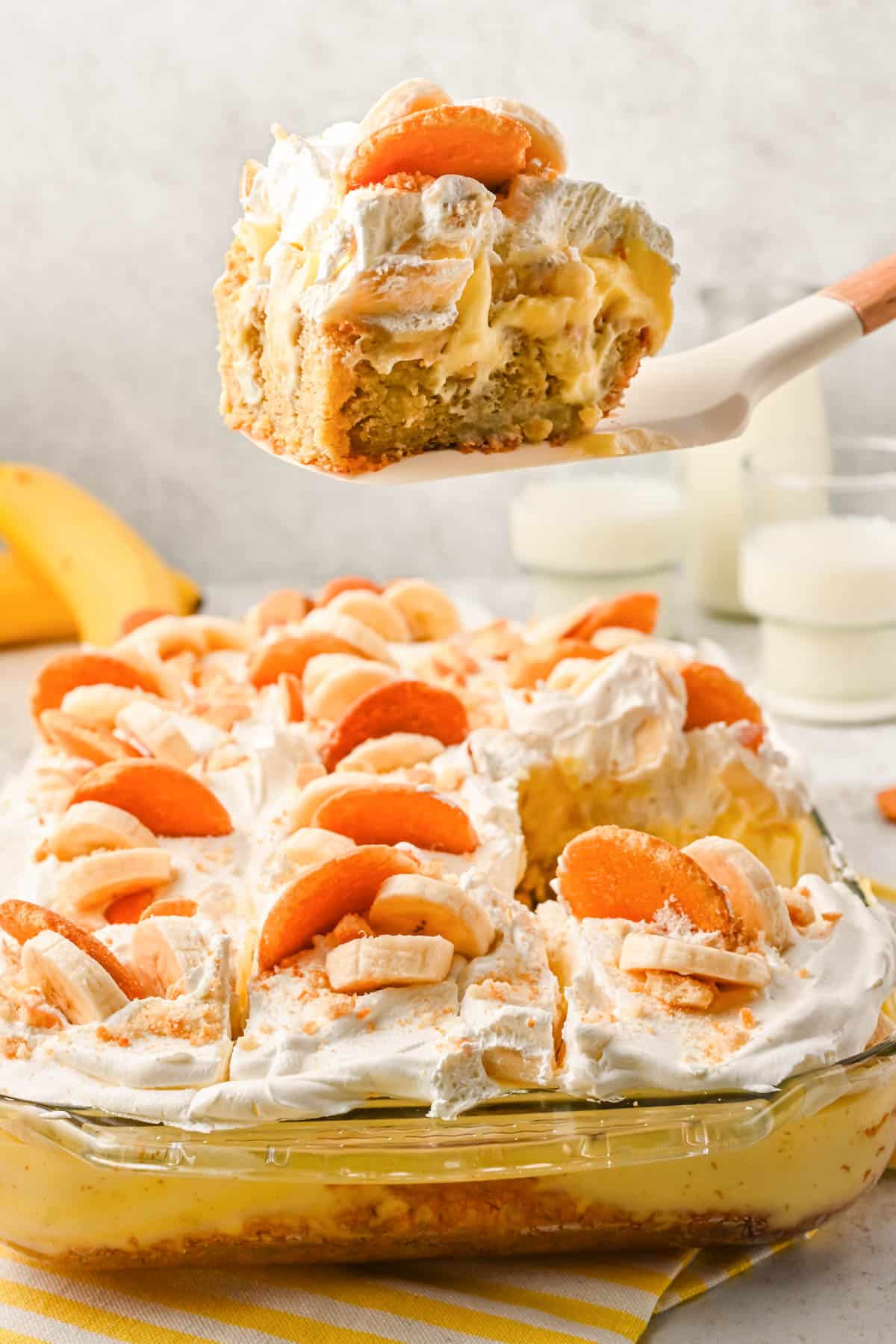 a slice of banana pudding poke cake being lifted out of a baking dish with a spatula