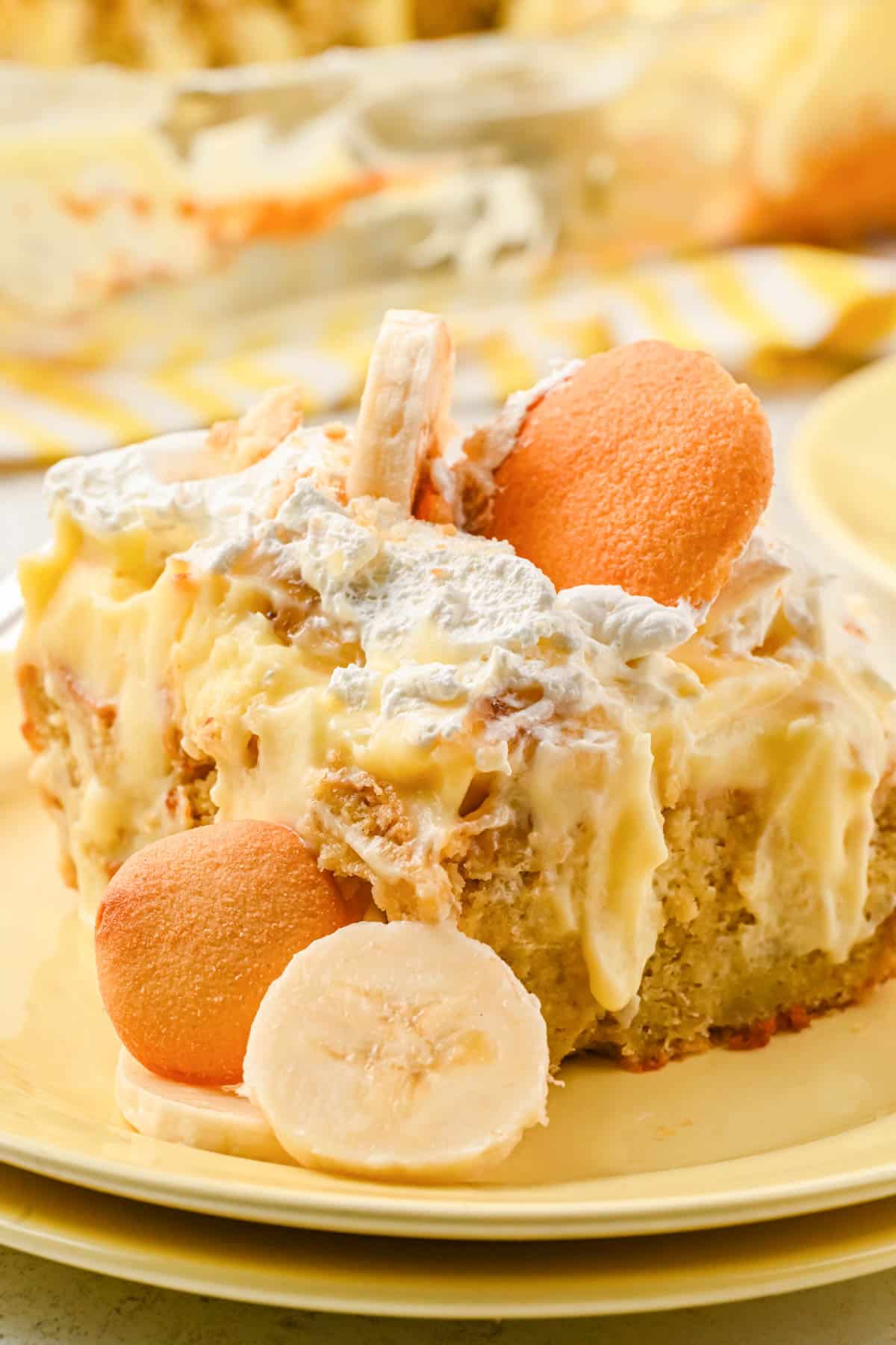 slice of banana pudding poke cake on a yellow plate with vanilla wafers and sliced bananas