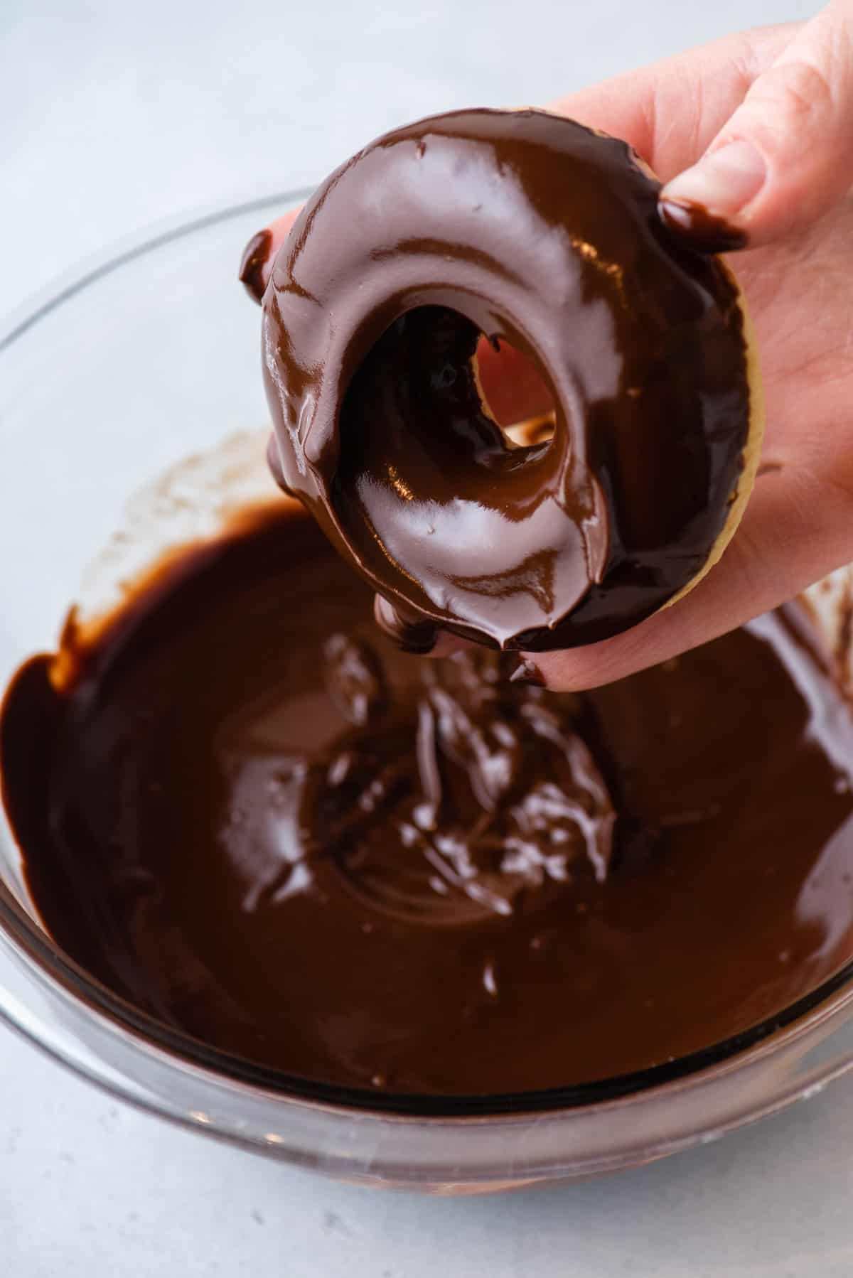 A hand dipping a donut into chocolate glaze