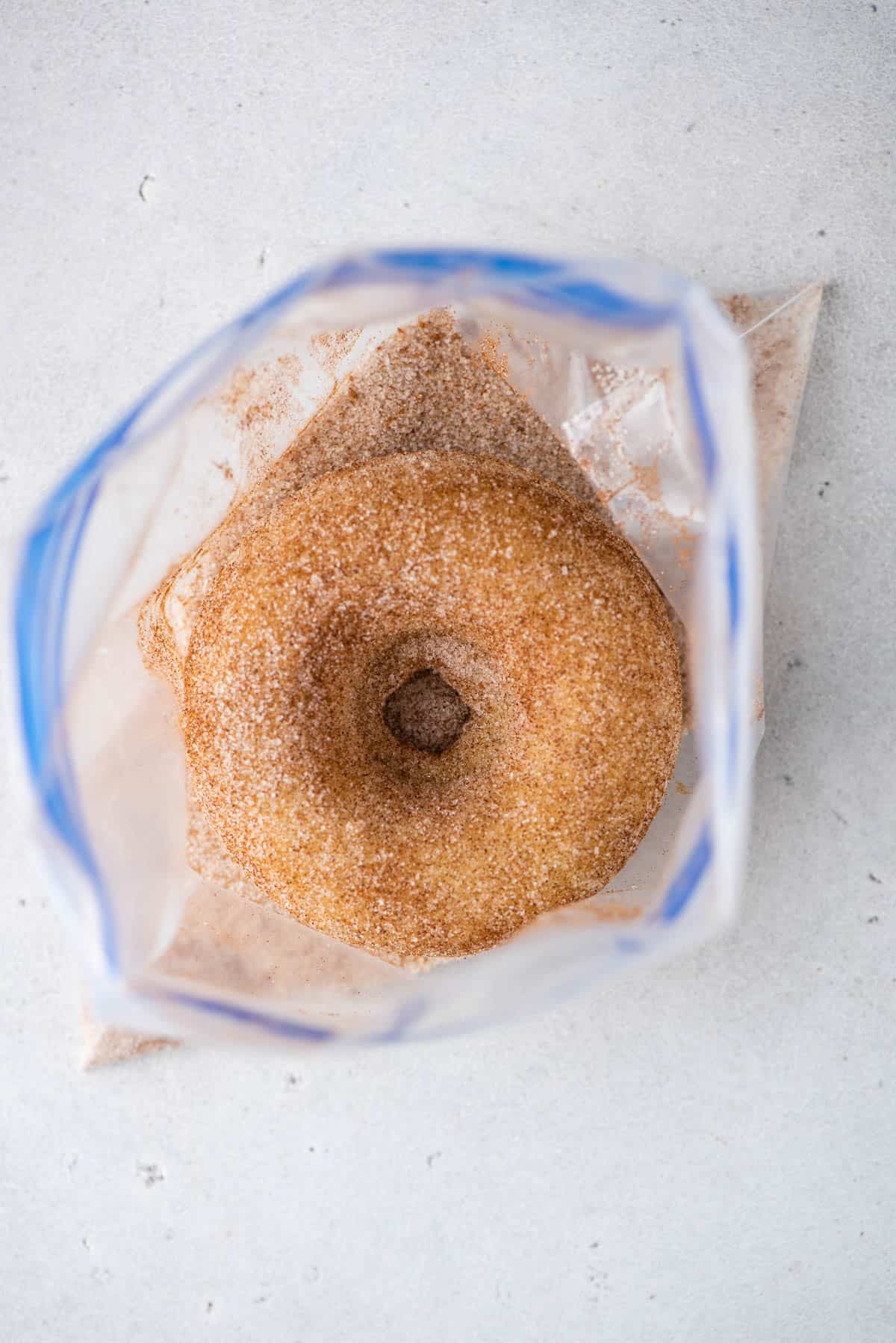 donut in a ziploc bag being coated in a cinnamon sugar mixture