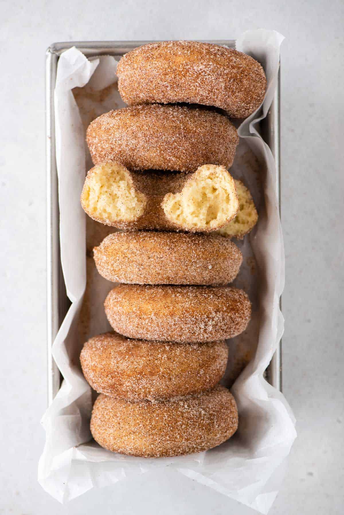 cinnamon donuts lined up in a loaf pan with white parchment paper underneath 