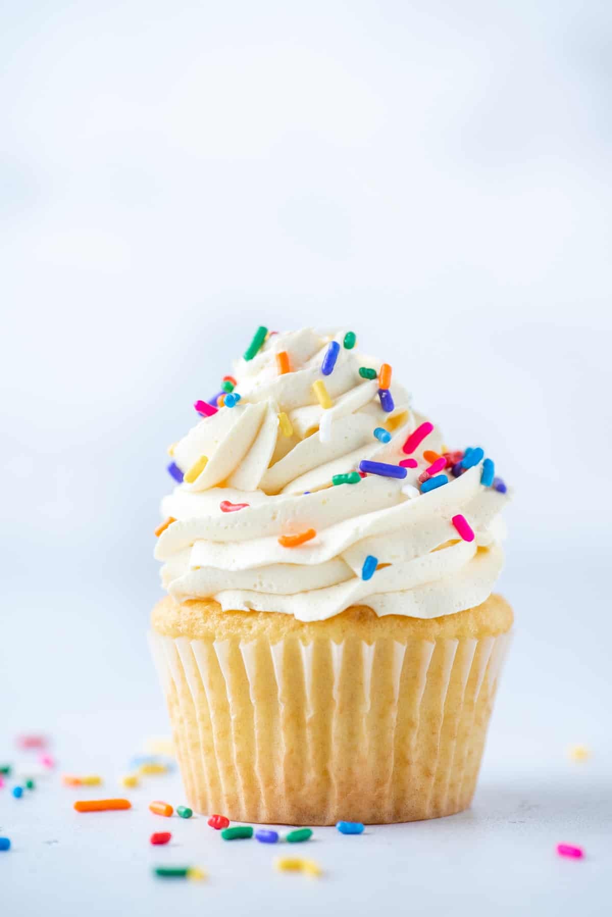 vanilla cupcake topped with cool whip frosting and sprinkles with sprinkles around it on a white surface