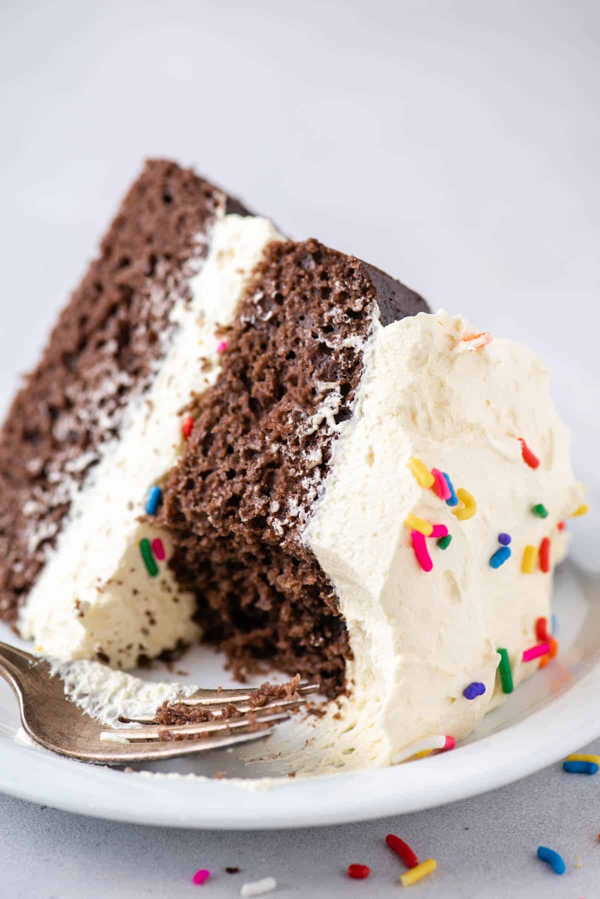 partially eaten chocolate cake topped with cool whip frosting and sprinkles on a while plate with a fork