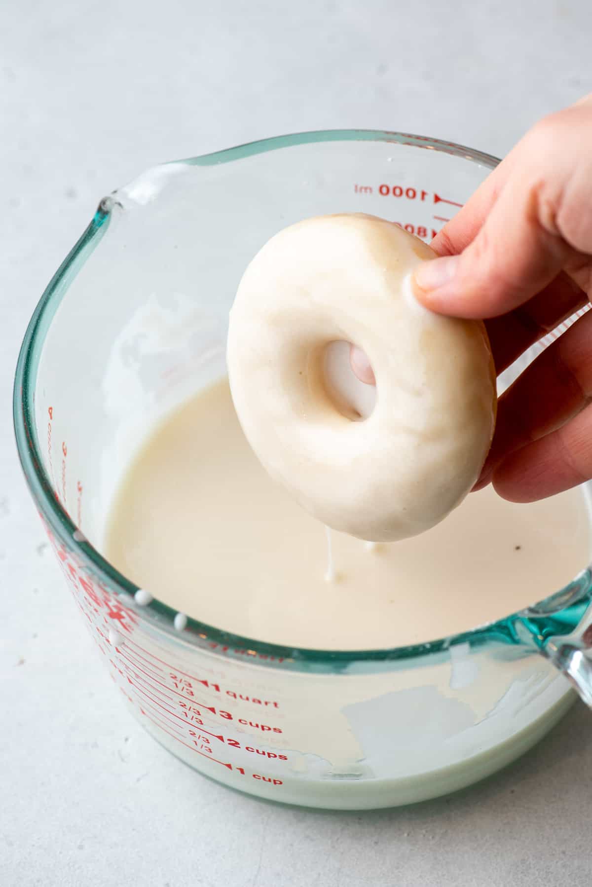 A hand dipping a donut into glaze