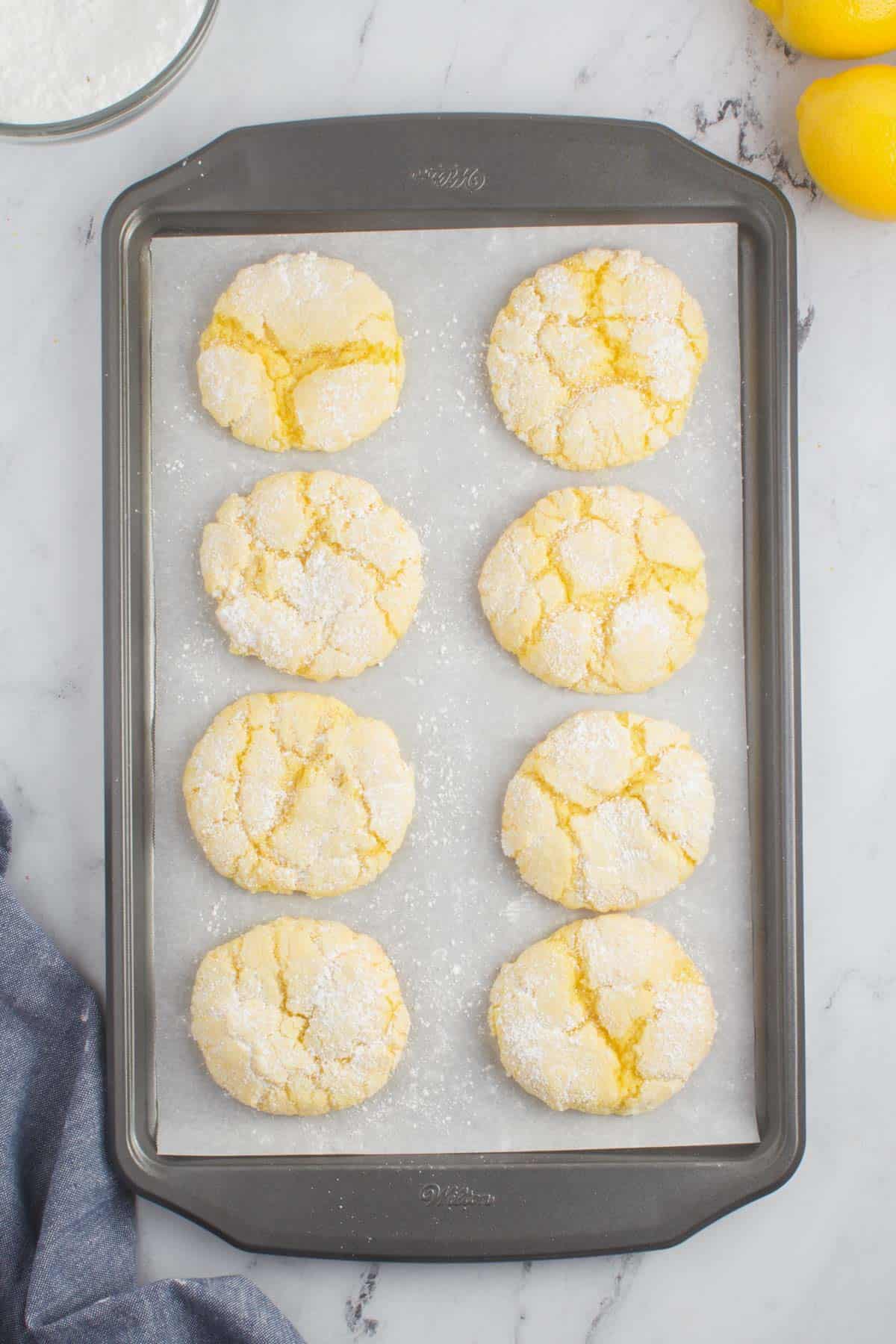 eight lemon cake mix cookies on a baking sheet lined with parchment paper sitting on a granite counter