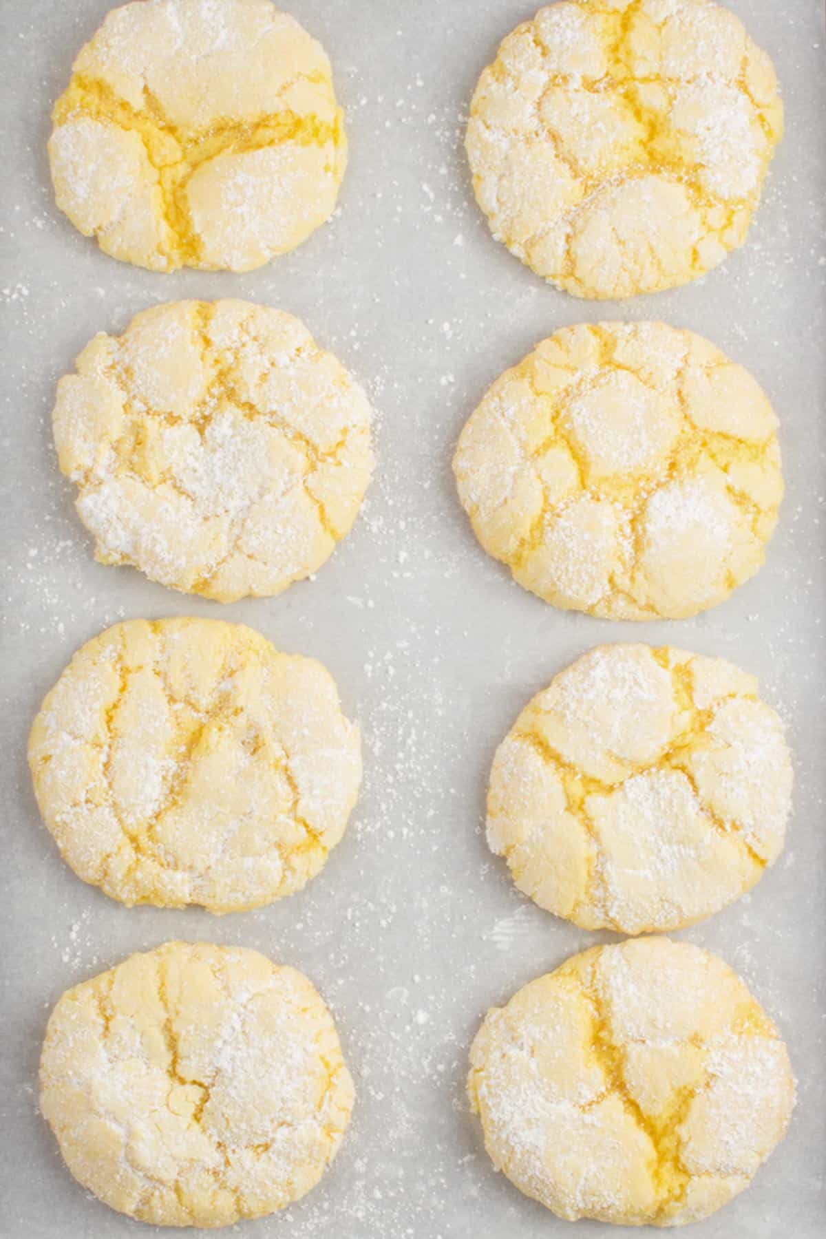 eight lemon cake mix cookies on a baking sheet lined with parchment paper sitting on a granite counter