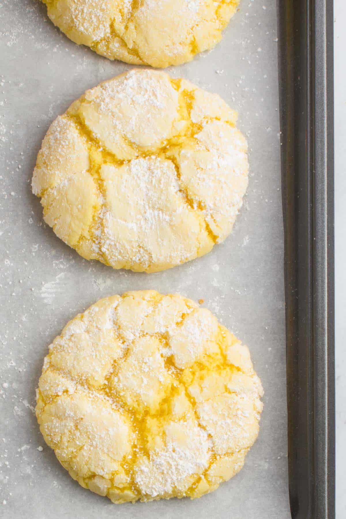 two lemon cake mix cookies on a baking sheet lined with parchment paper