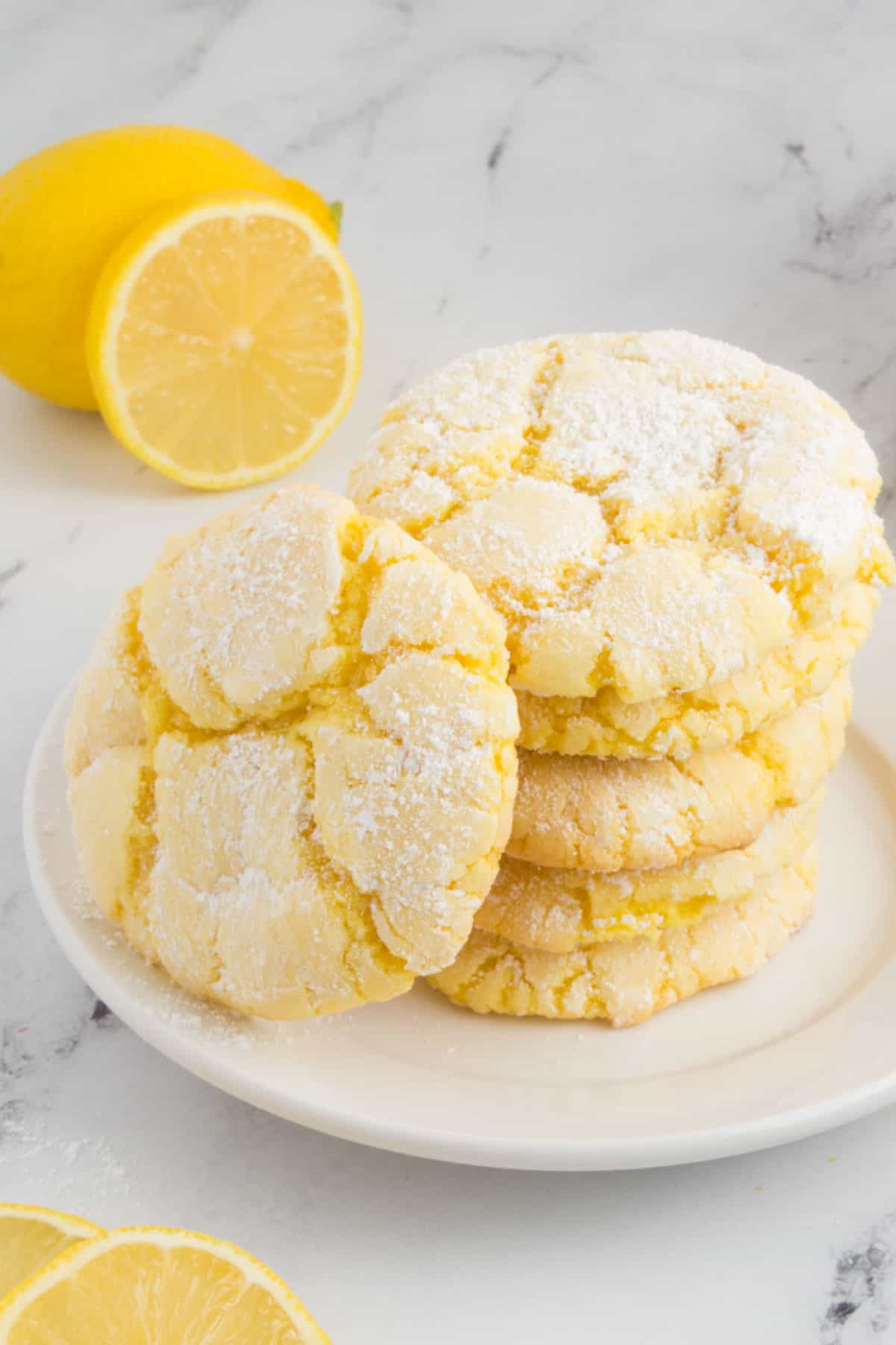 lemon cookies arranged on a white plate sitting on a granite countertop with sliced lemons around the plate