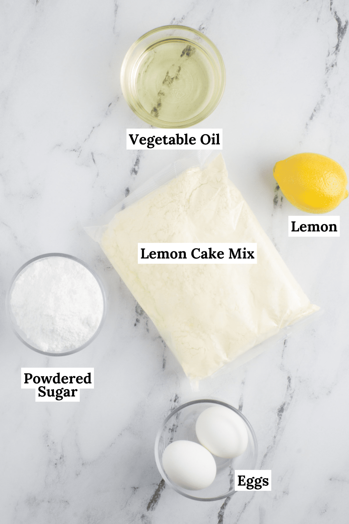 ingredients for lemon cake mix cookies arranged on a countertop including eggs, a bag of cake mix, powdered sugar, a lemon and vegetable oil