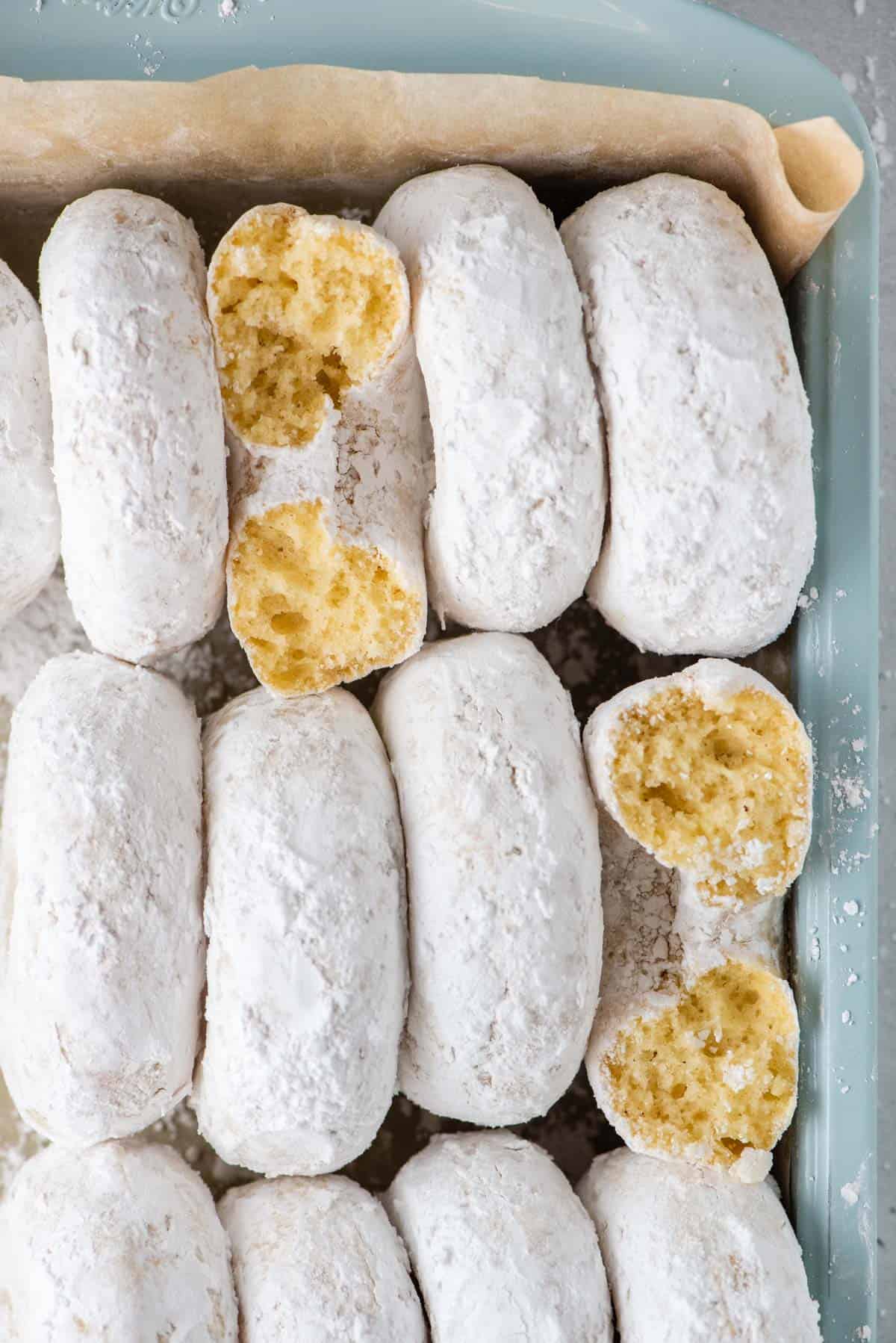 Powdered Sugar Donuts lined vertically side by side in a teal baking dish lined with brown paper
