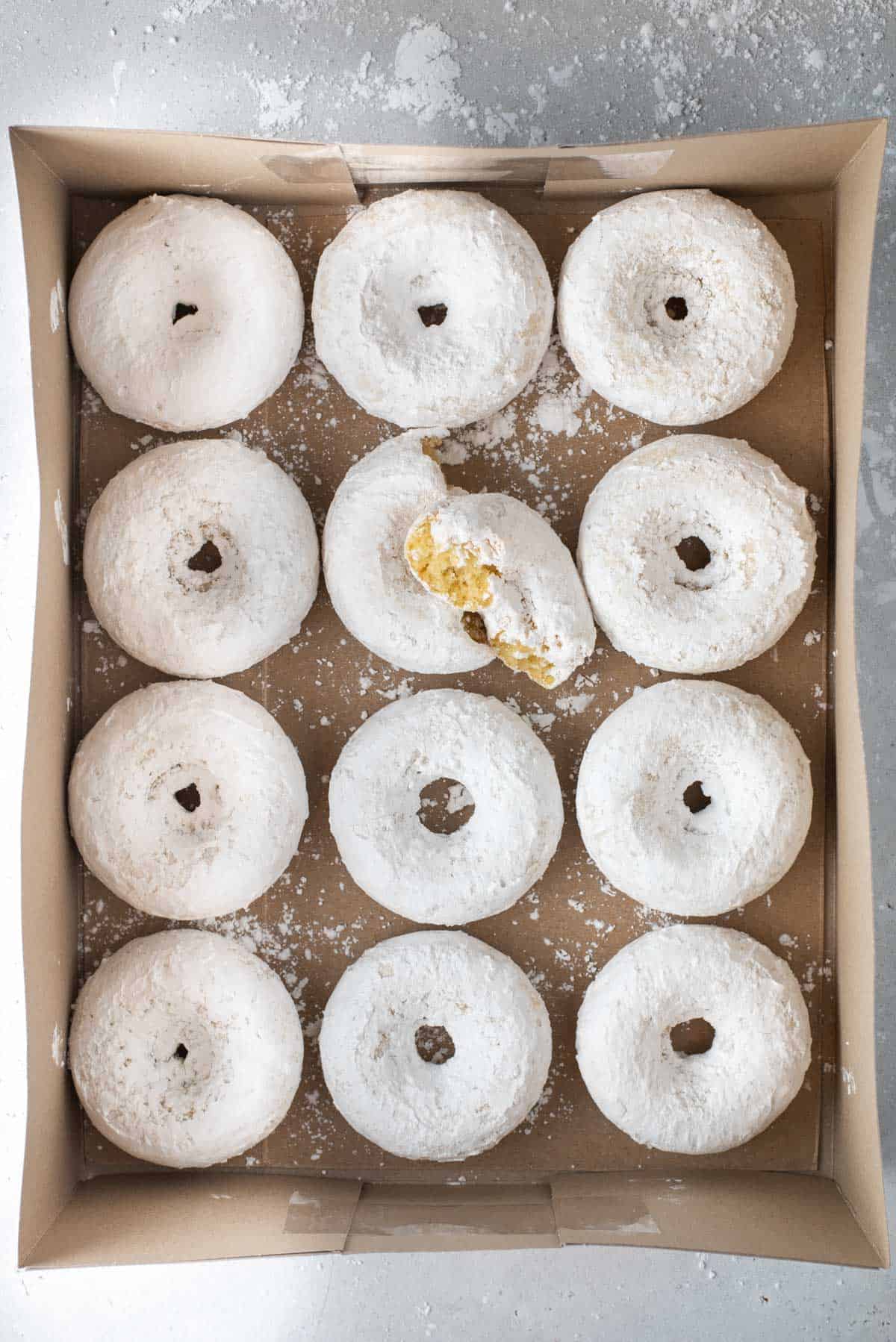 powdered sugar donuts laying flat in rows in a box sitting on a counter top