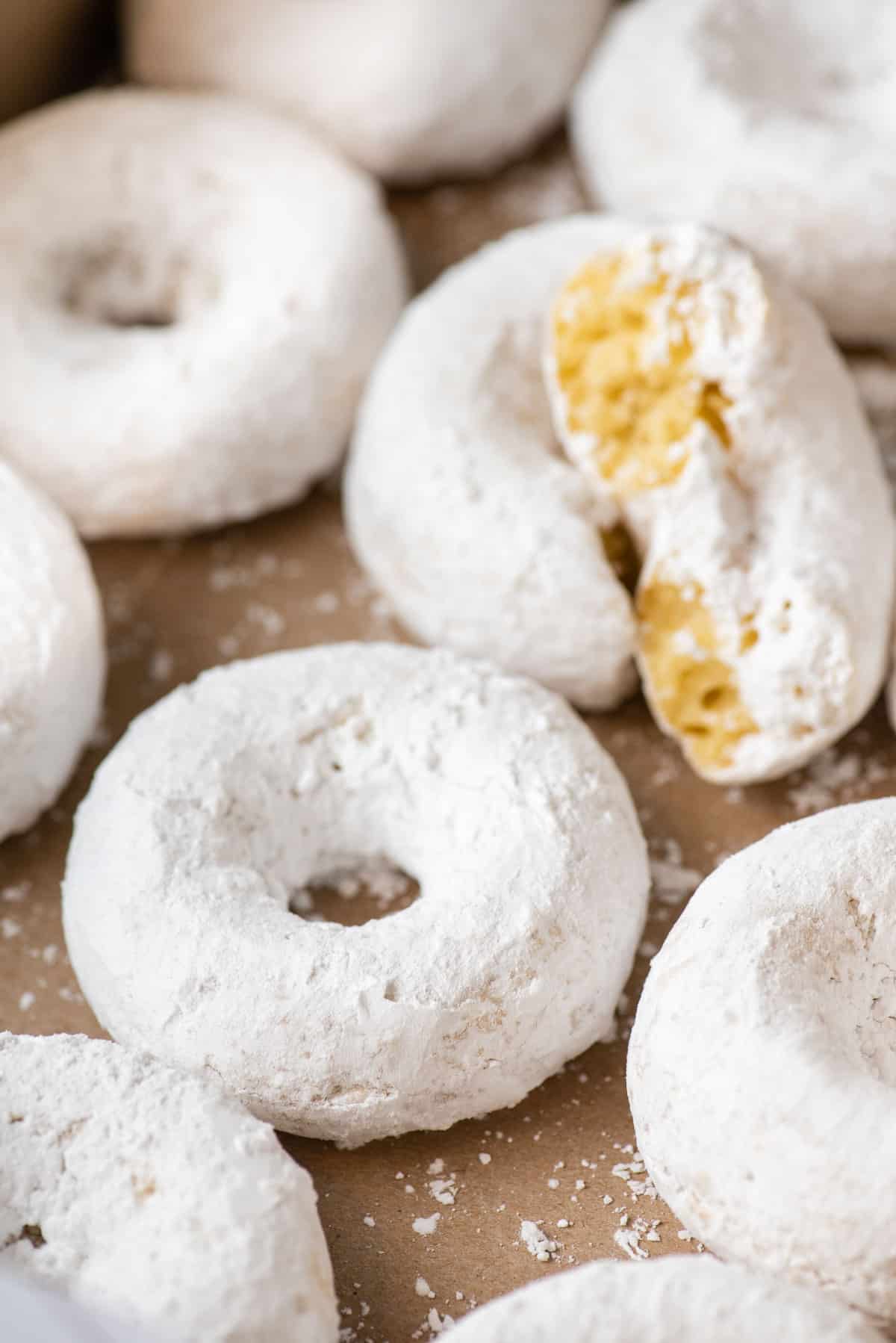 close up of powdered sugar donuts arranged on brown paper