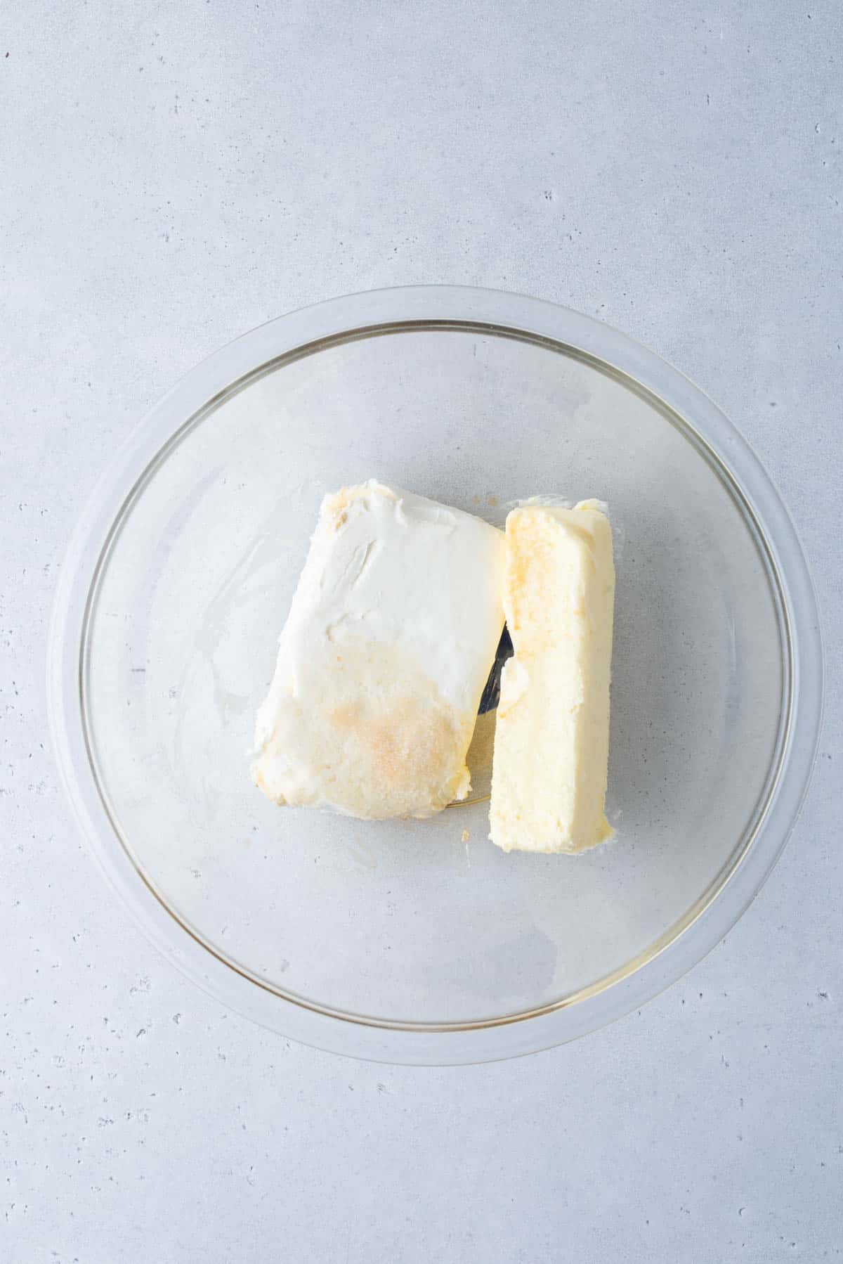 cream cheese and a stick of butter in a clear glass bowl on a white surface