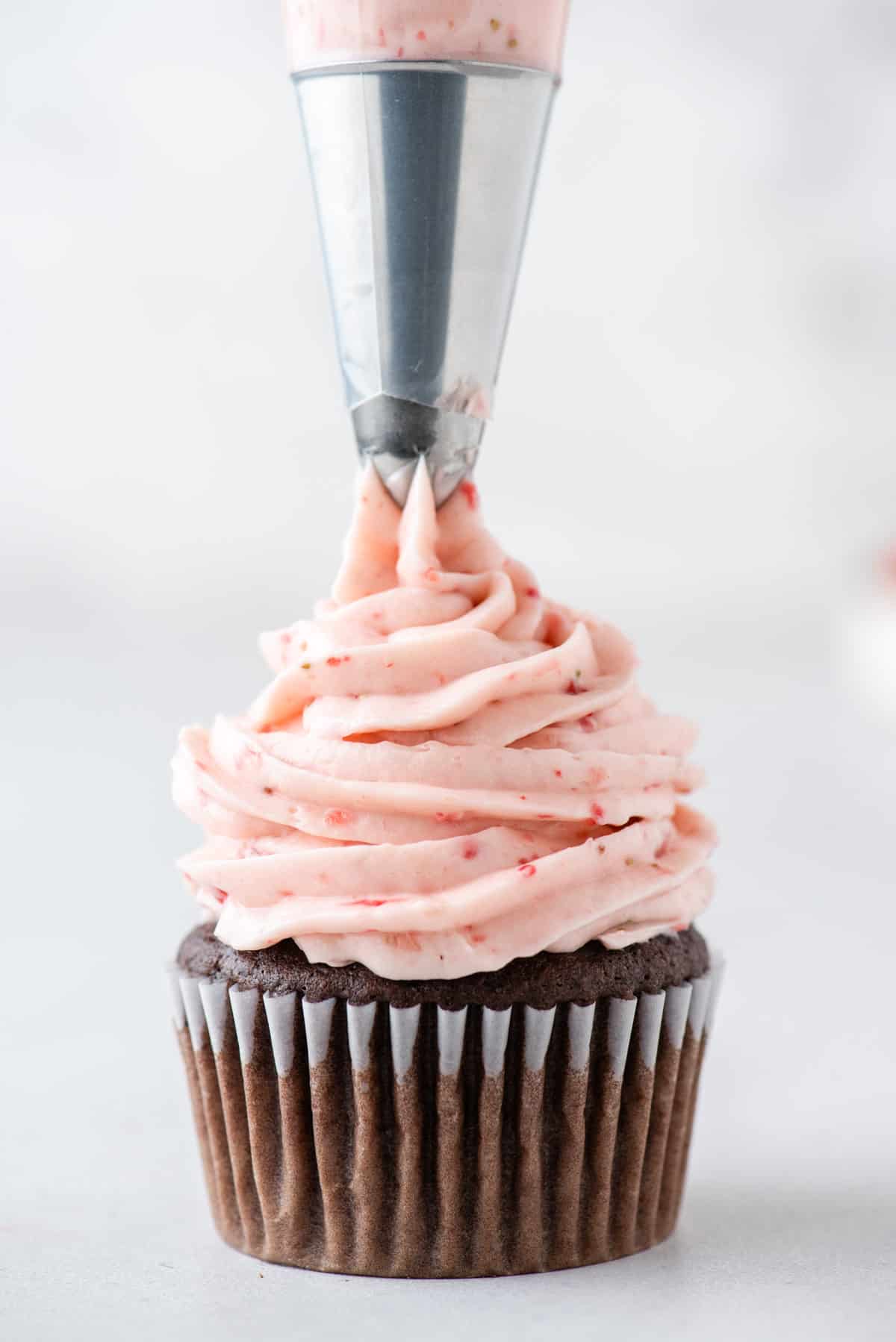 chocolate cupcake sitting on a white surface with strawberry frosting being piped on top