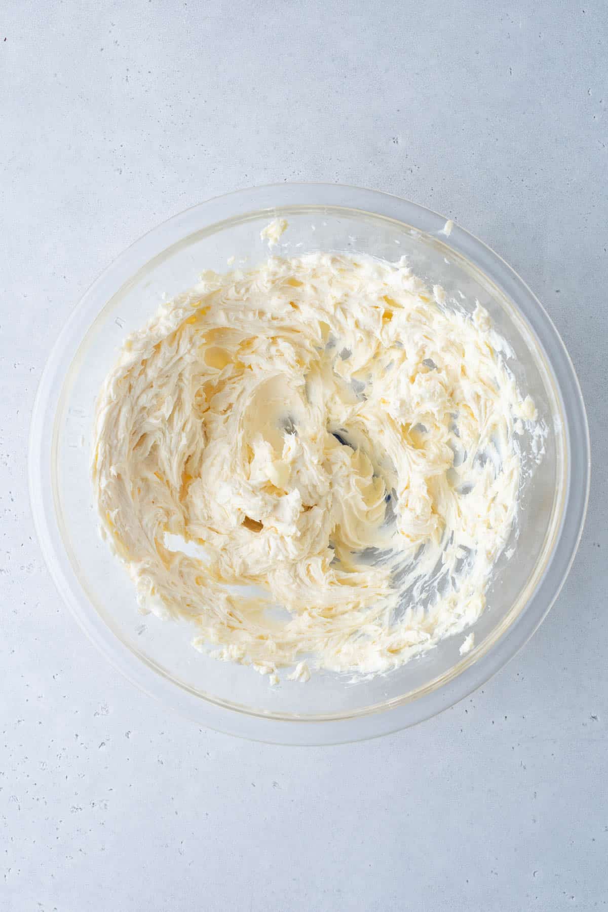 cream cheese and butter mixed together in a clear glass bowl on a white surface