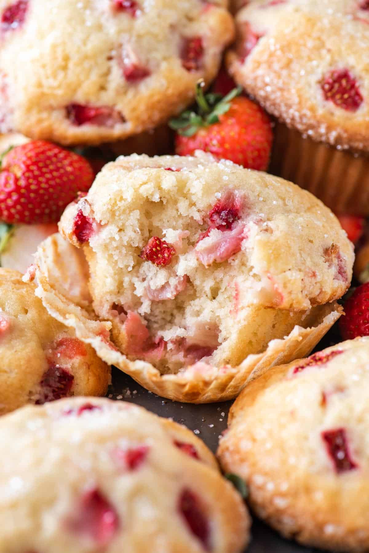close up of strawberry muffins with one partially eaten, arranged with fresh strawberries in between
