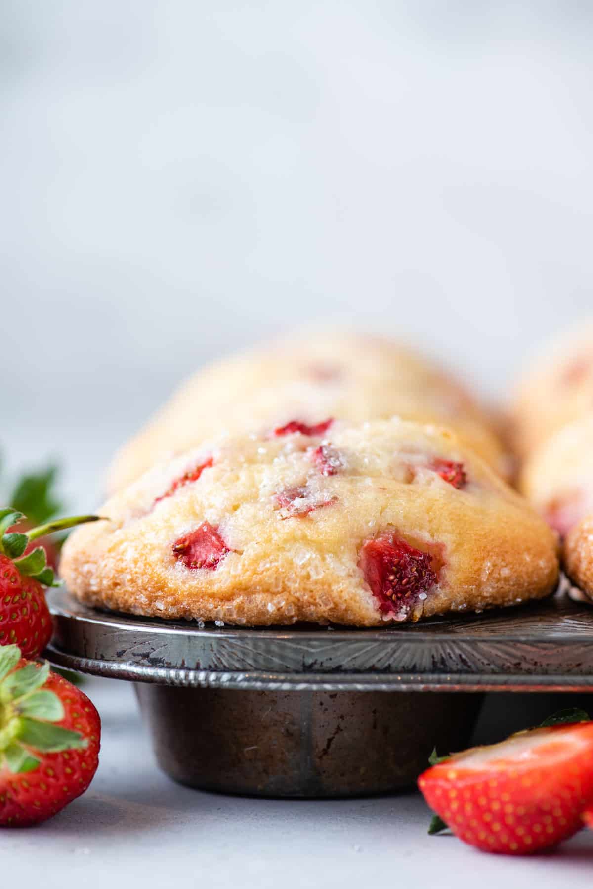 strawberry muffins in a muffin pan with fresh strawberries arranged around it