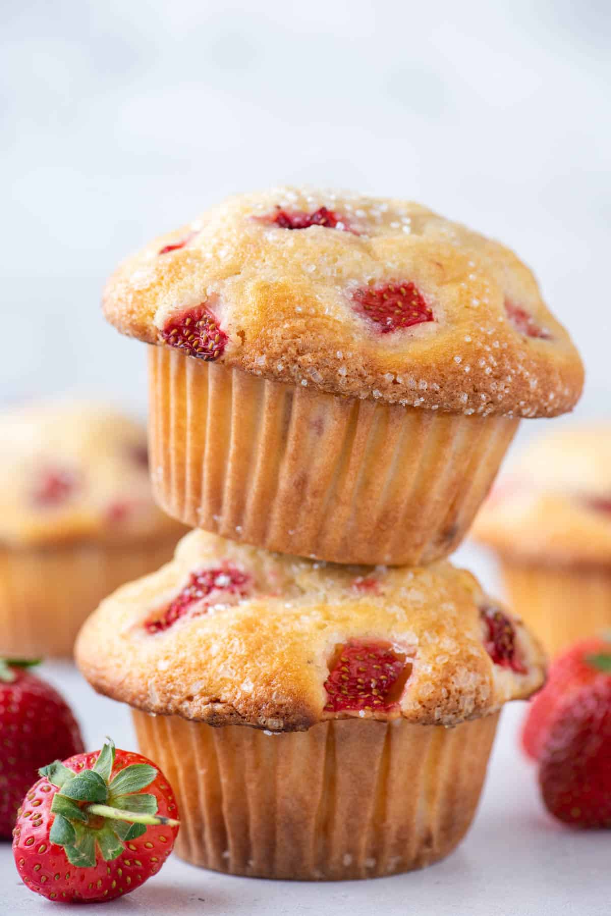 two strawberry muffins stacked with fresh strawberries around them