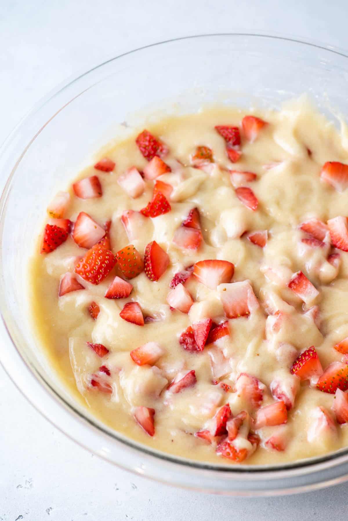 strawberry muffin batter in a clear glass bowl on a white surface