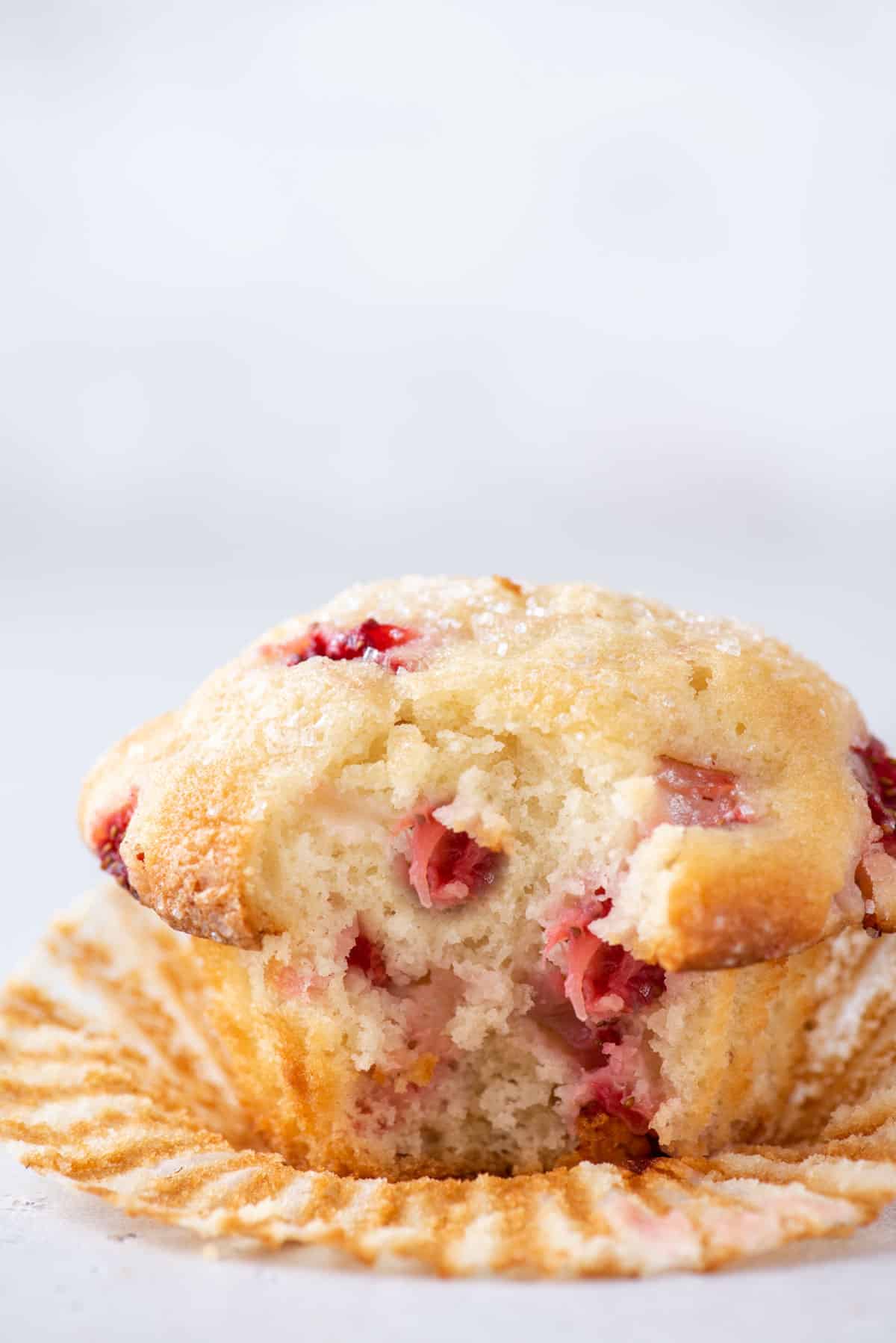 strawberry muffin with one bite taken out sitting on an open paper muffin cup