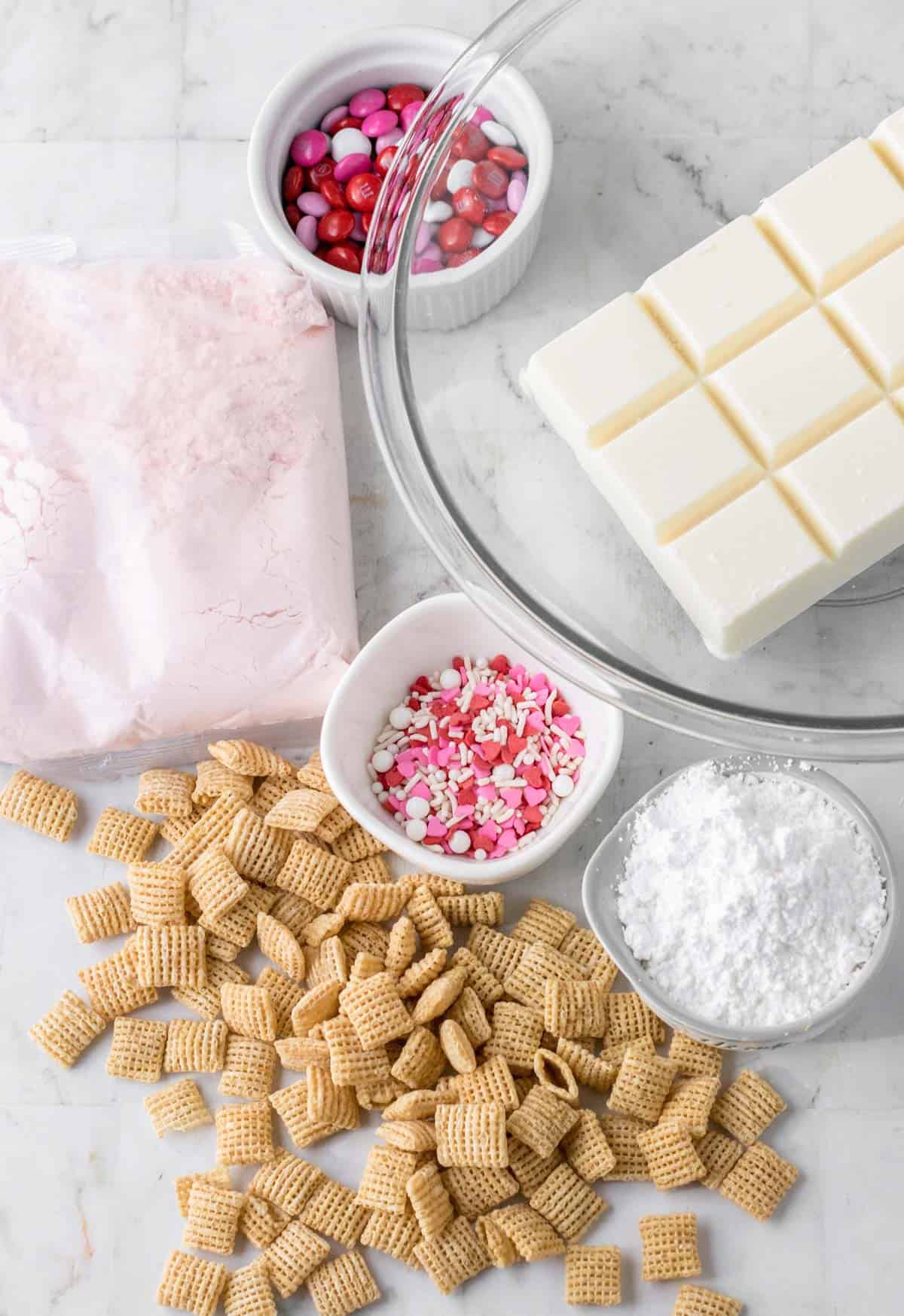 Ingredients for Valentine's day puppy chow in separate bowls including Rice Chex cereal, White almond bark, Strawberry cake mix, Powdered sugar, and Valentine’s Day Sprinkles
Valentine’s Day M&Ms