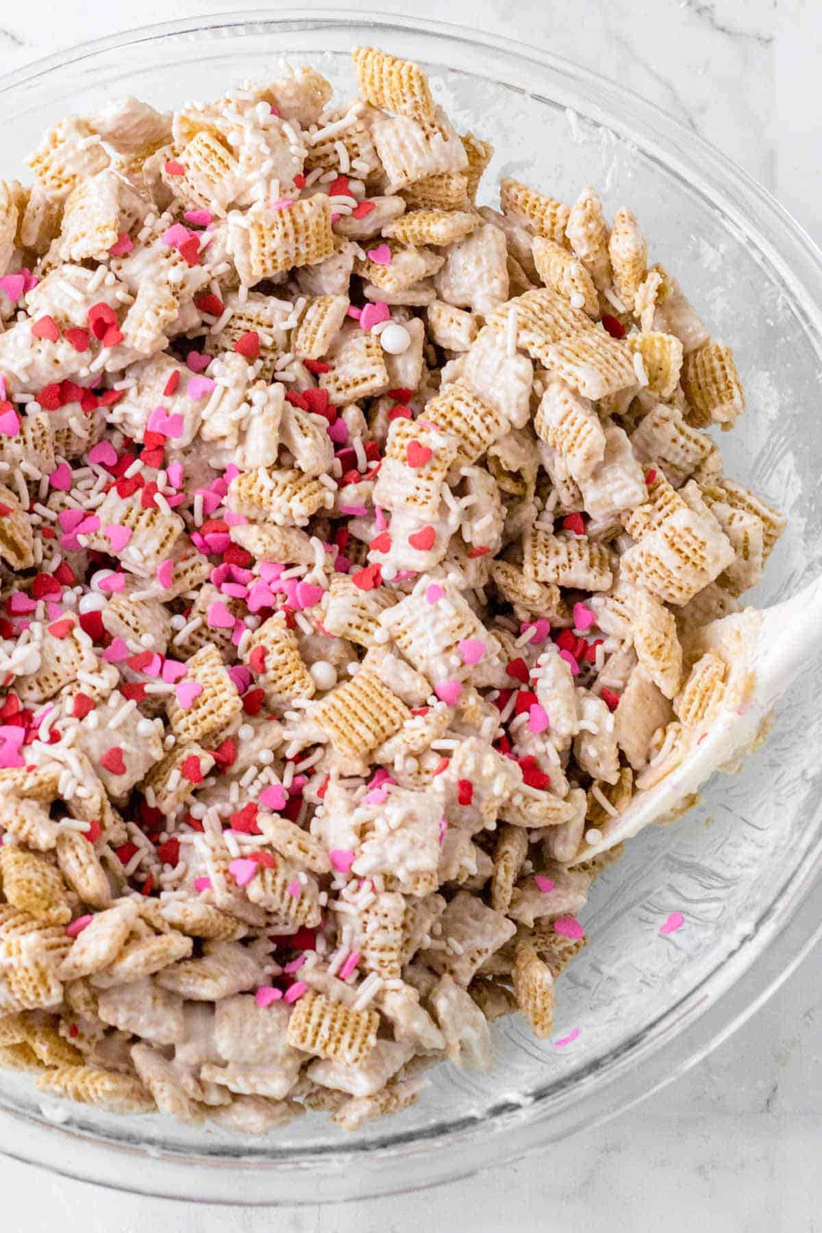 Valentine's Day Puppy Chow recipe in a clear bowl sitting on a white countertop