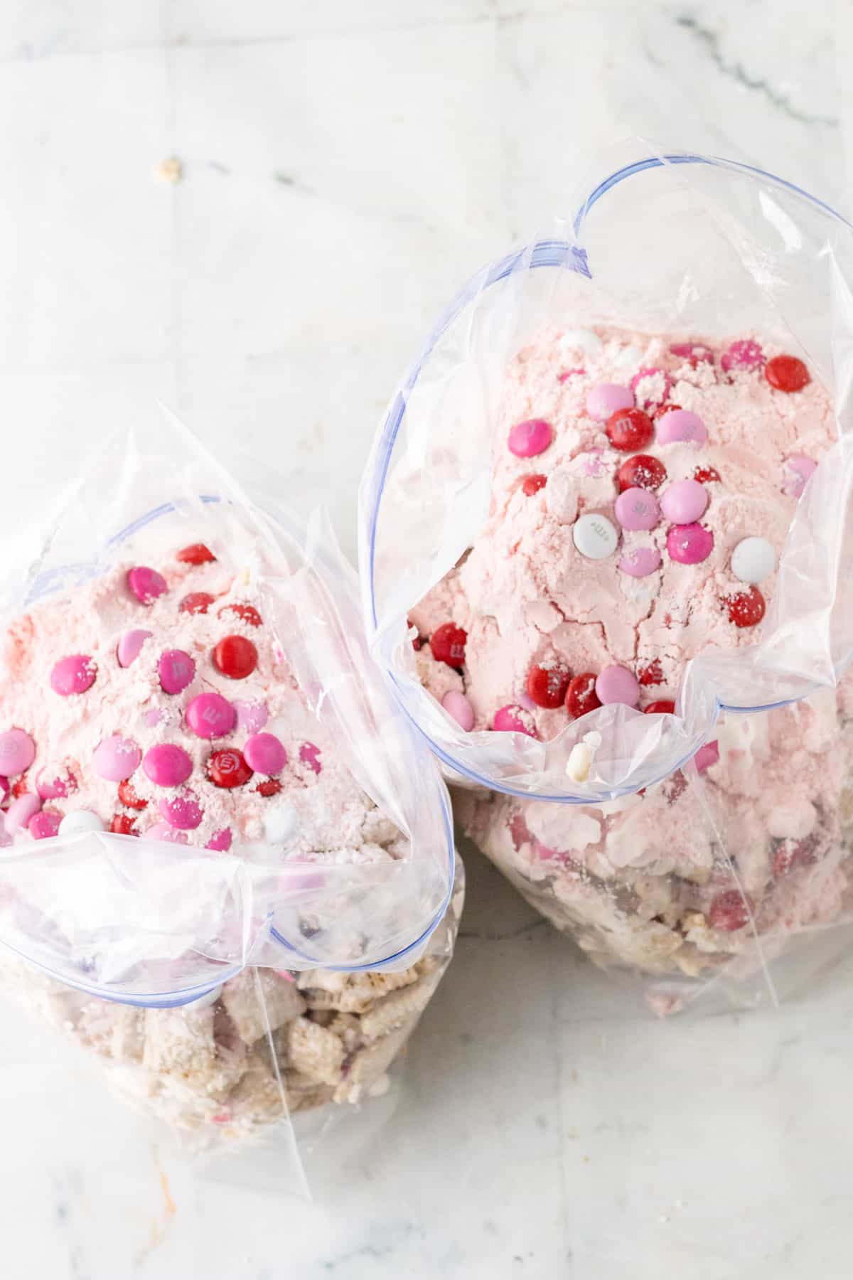 Valentine's Day Puppy Chow mixture inside large plastic bags sitting on a white counter.