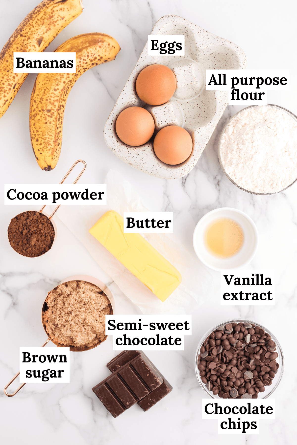 the ingredients for banana brownies including a bowl of chocolate chips, semi-sweet chocolate bars, brown sugar, vanilla extract, butter, bananas, eggs, all purpose flour and cocoa powder