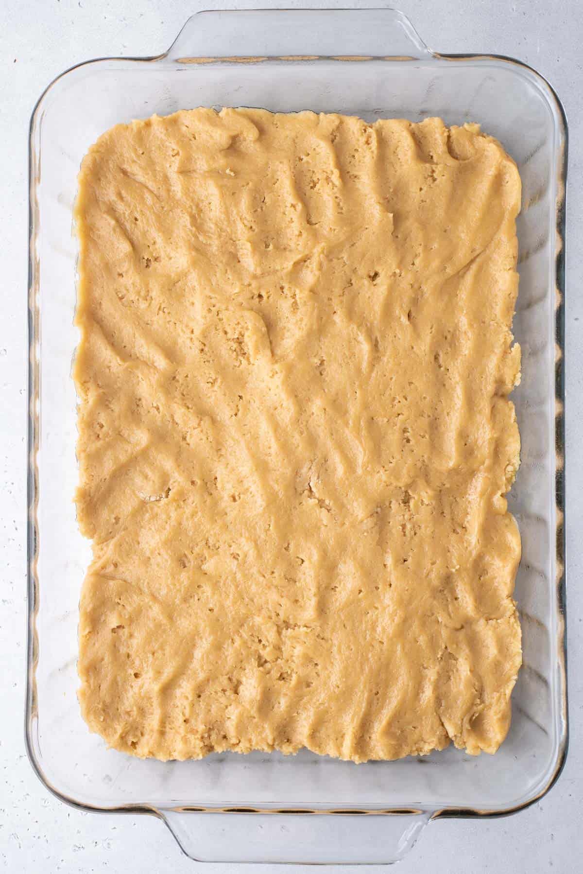 blondie dough pressed into a flat layer in a clear baking dish