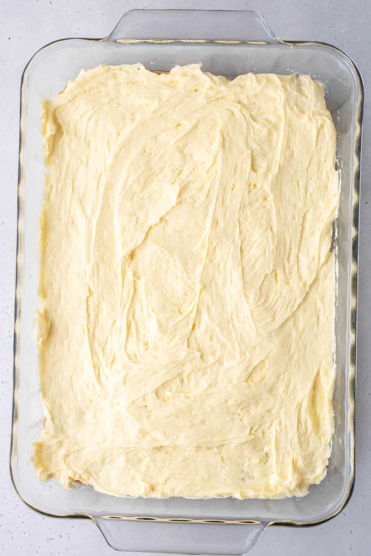 a clear baking dish with the first two layers of banana pudding brownies in it, the blondie layer and the banana pudding mix later