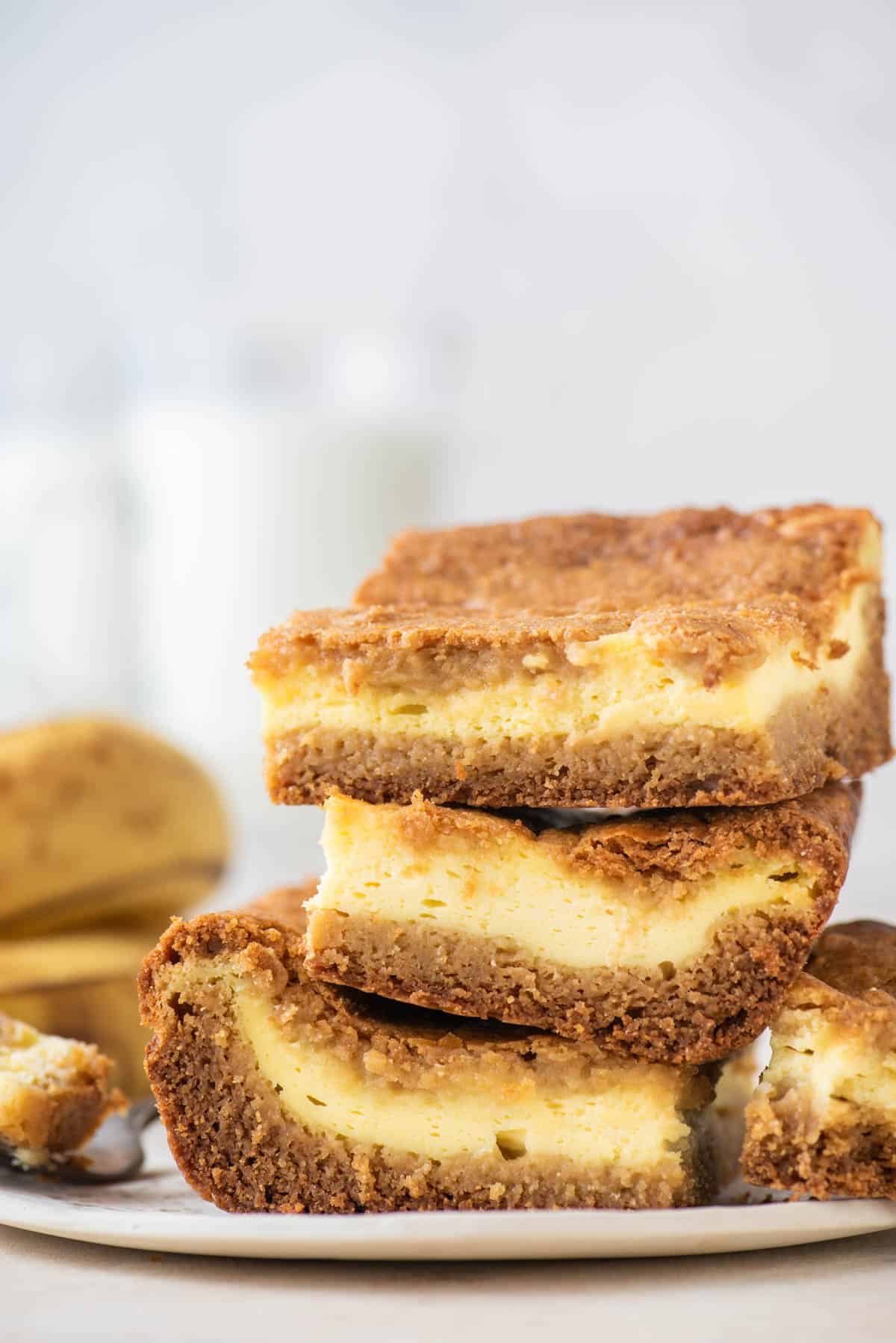 three banana pudding brownies stacked on a plate with bananas in the background
