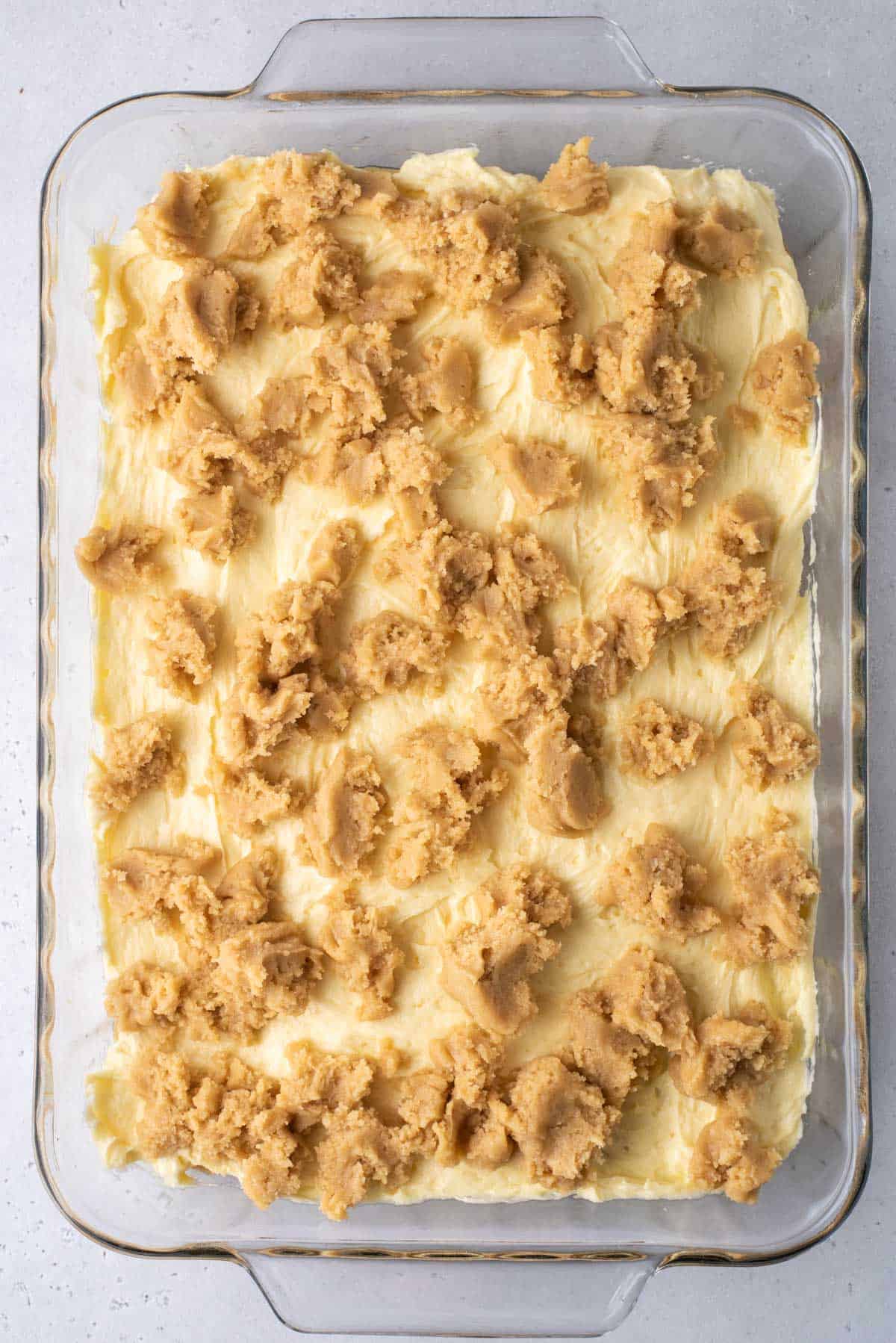 a clear baking dish with the layers of banana pudding brownies in it, the blondie layer, the banana pudding mix, and another layer of blondie mix before it has been baked