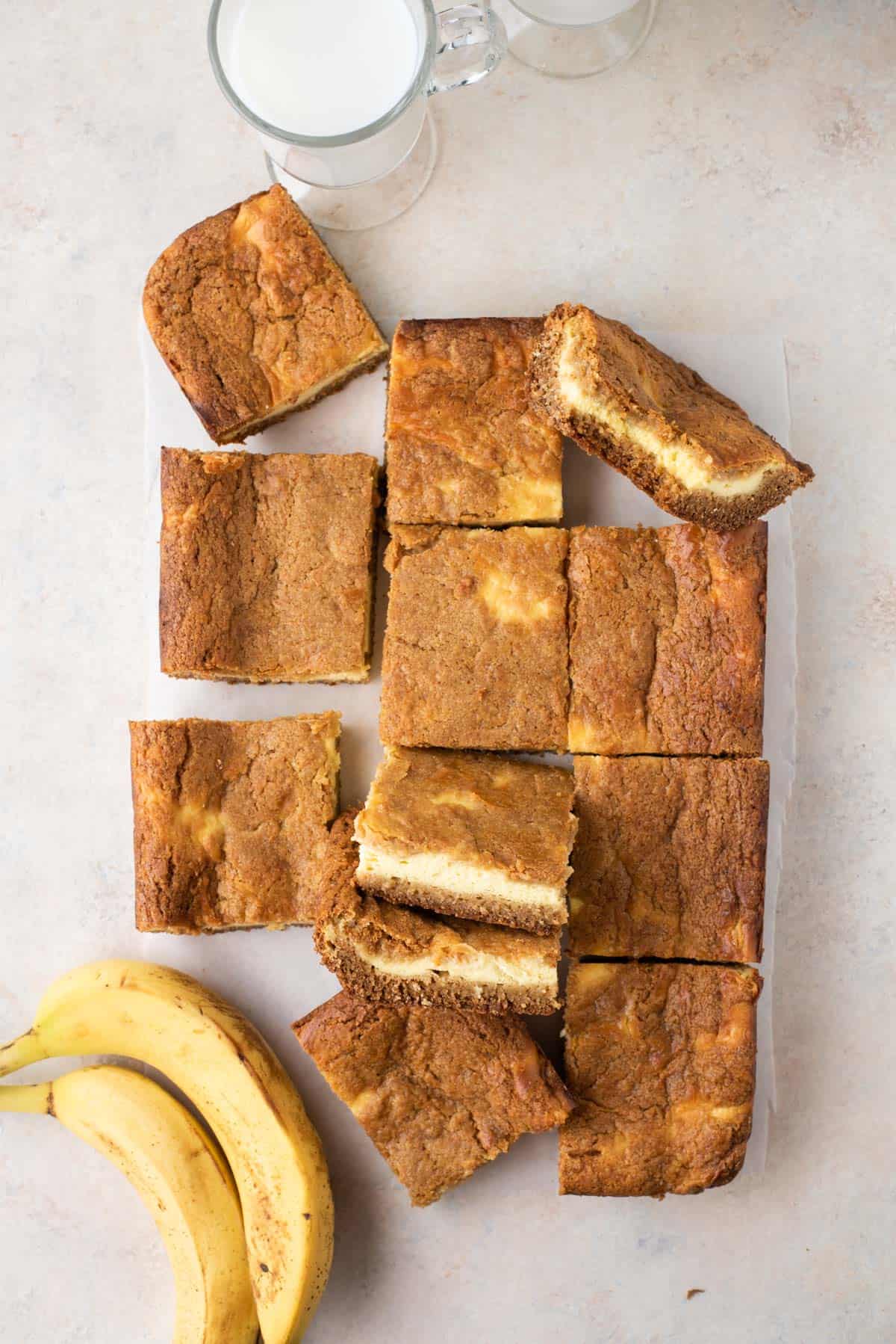 Banana pudding brownies arranged on a counter with bananas and cup of milk
