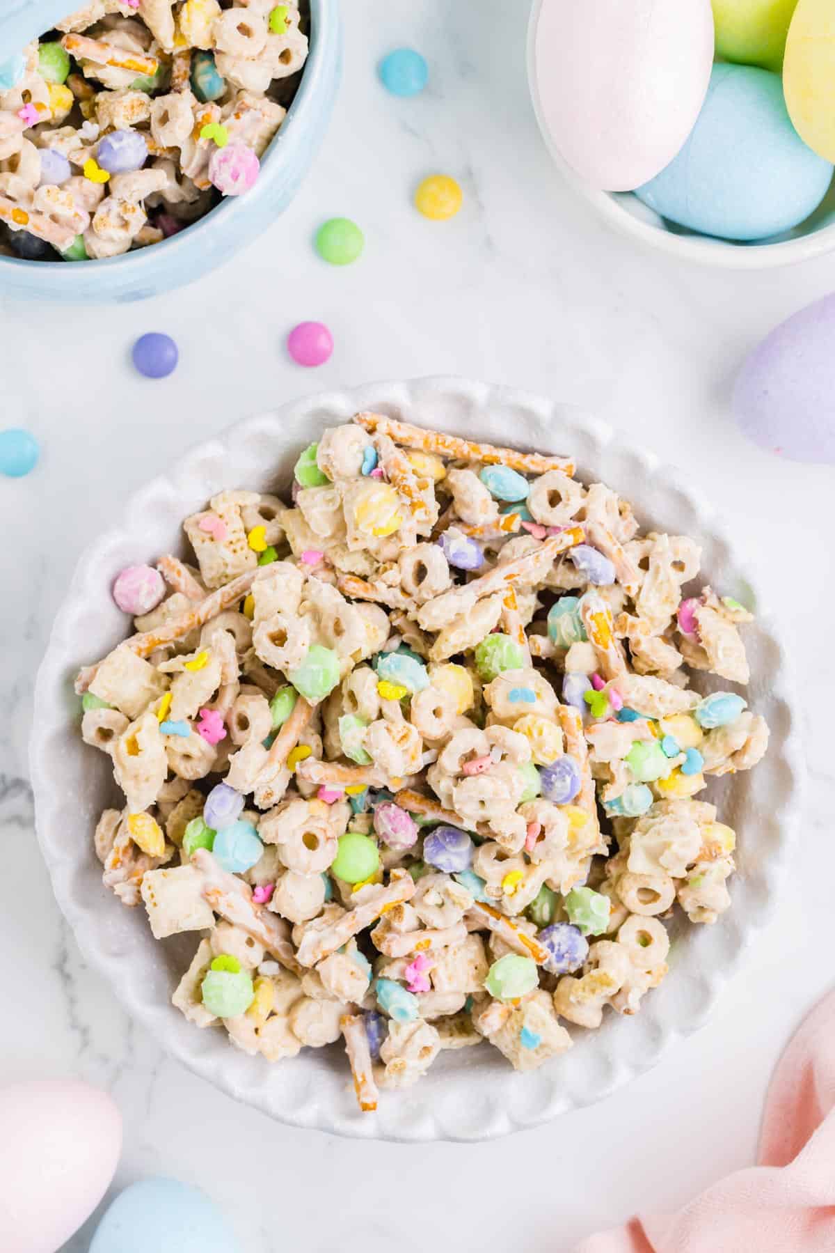 a large white bowl of bunny bait snack mix surrounded by a smaller bowl of bunny bait and a bowl of easter eggs
