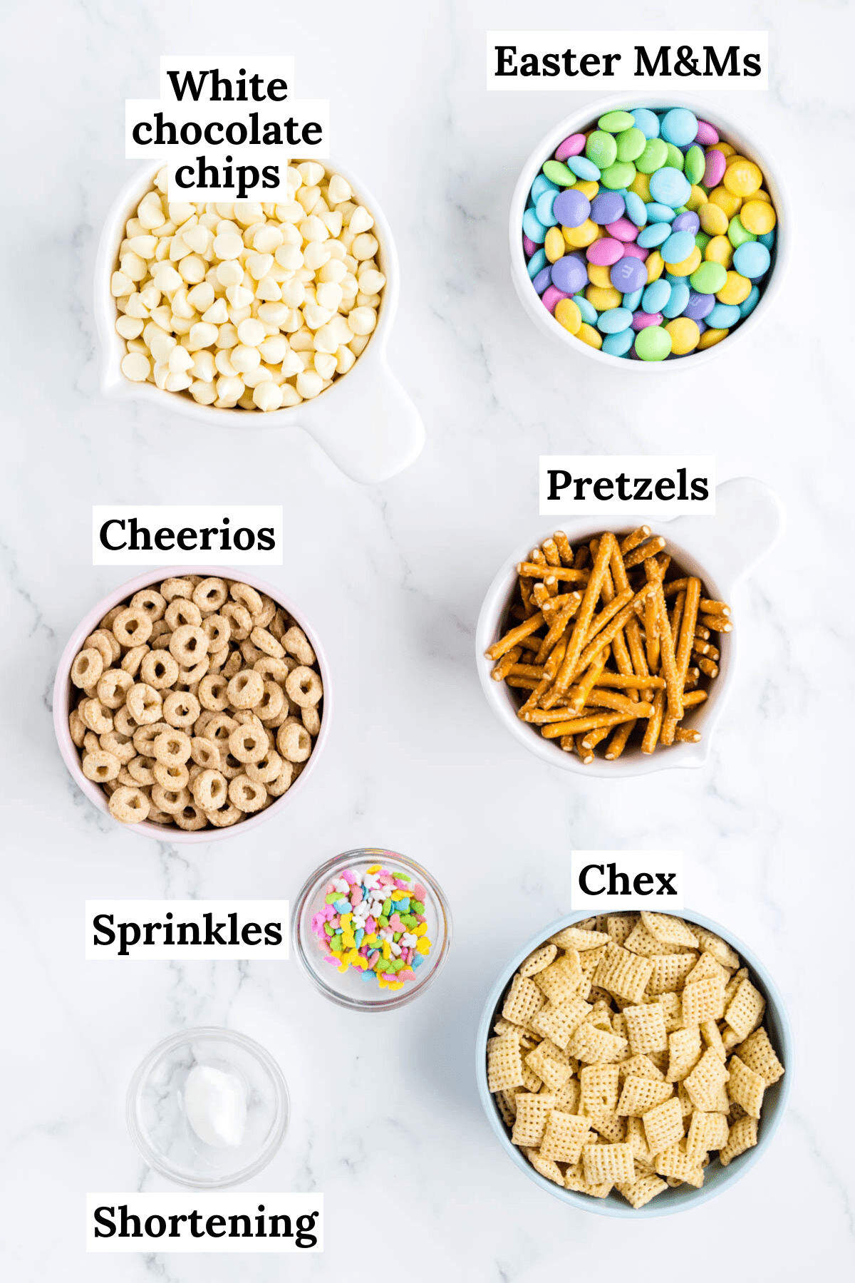ingredients for bunny bait including rice chex cereal, honey nut cheerios, pretzel sticks, easter M&Ms, white chocolate chips, vegetable shortening, and easter sprinkles