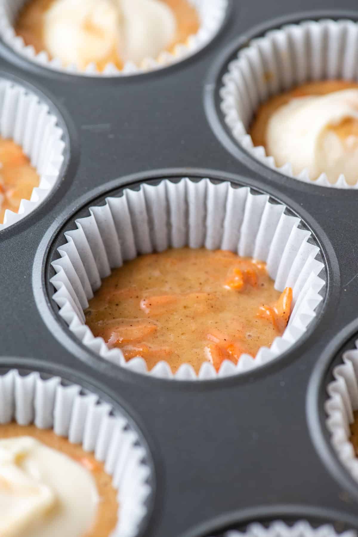 carrot cake muffin batter in the bottom of a paper liner in a muffin pan