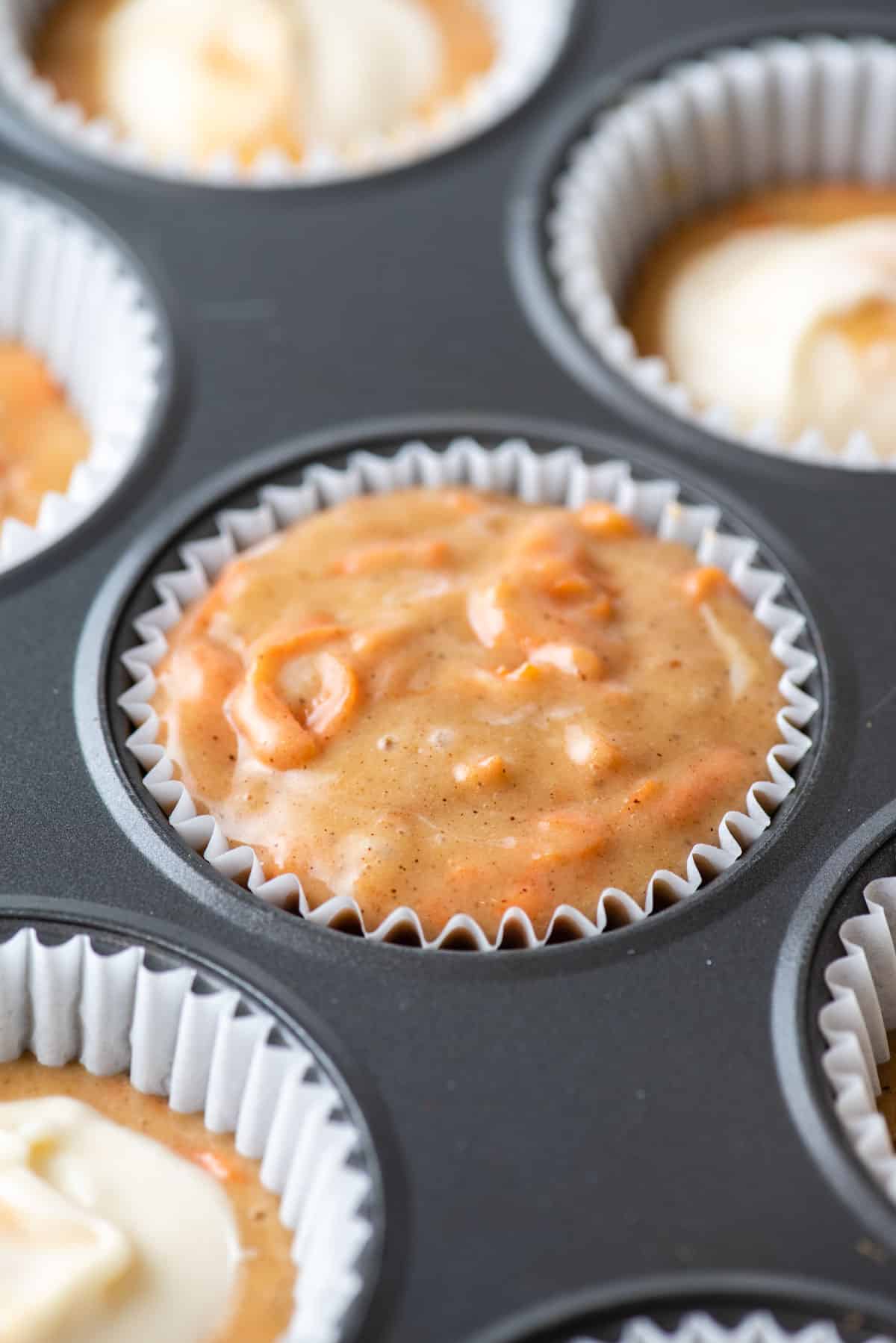 a muffin pan with a paper liner filled with carrot cake muffin batter
