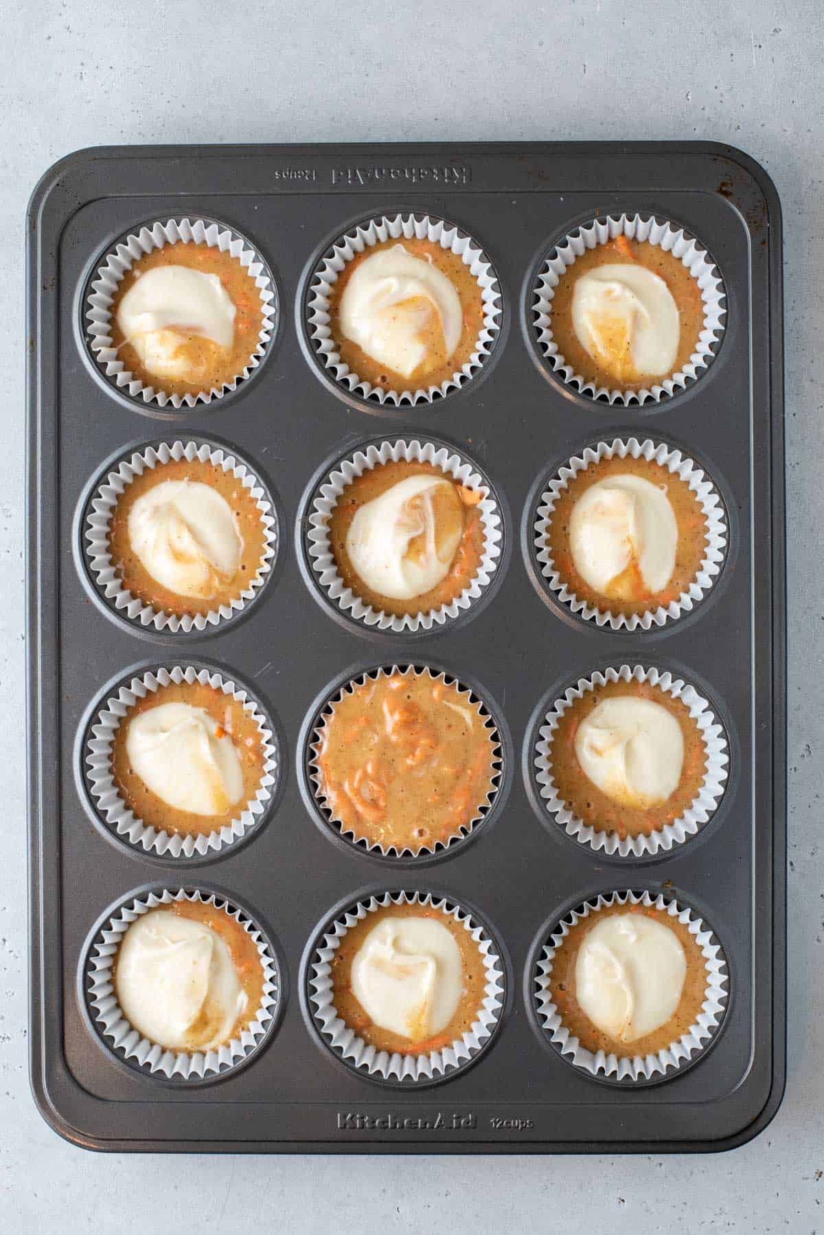 a muffin pan filled with paper lines and carrot cake muffin batter with cream cheese filling
