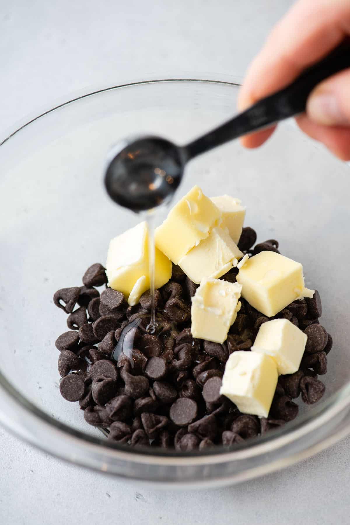 chocolate chips and butter in a clear glass bowl with corn syrup being poured in